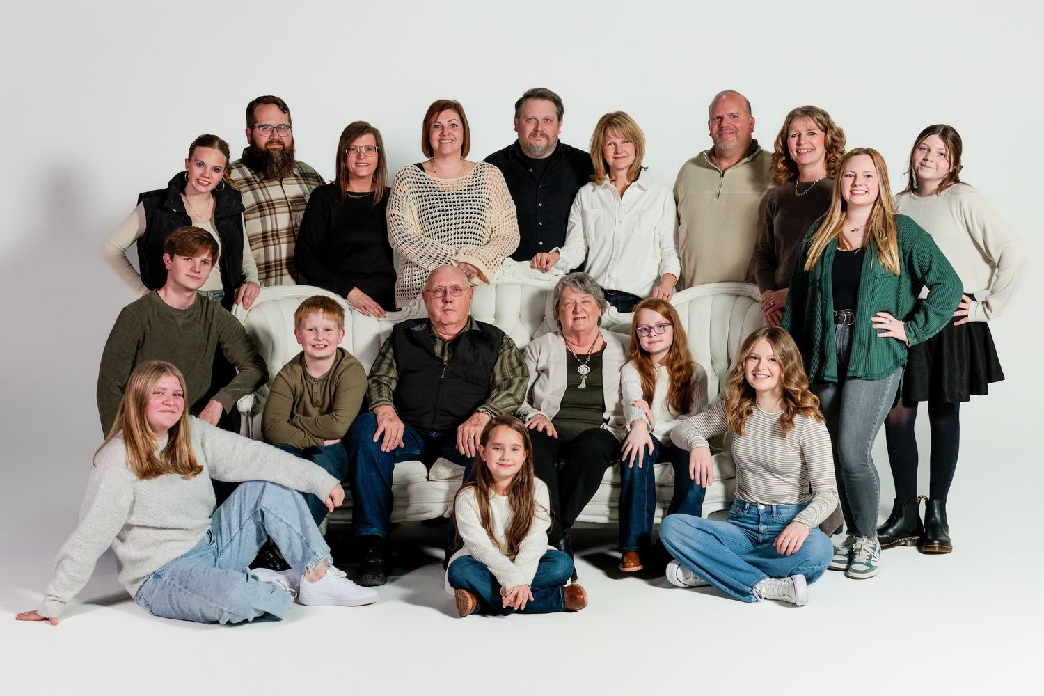 Multi-generational family photo in casual attire posed together in a studio setting with white background.