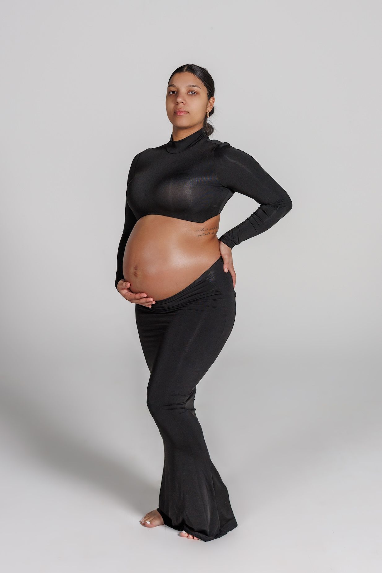 Pregnant person wearing black flowing ensemble poses gracefully against white background during maternity photoshoot.