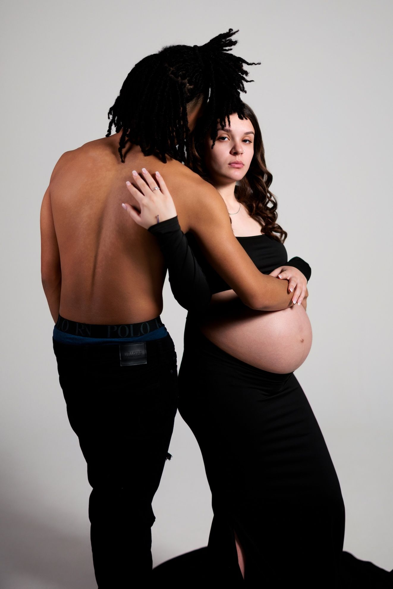 Intimate maternity photo showing silhouette of couple embracing in black clothing against light background.