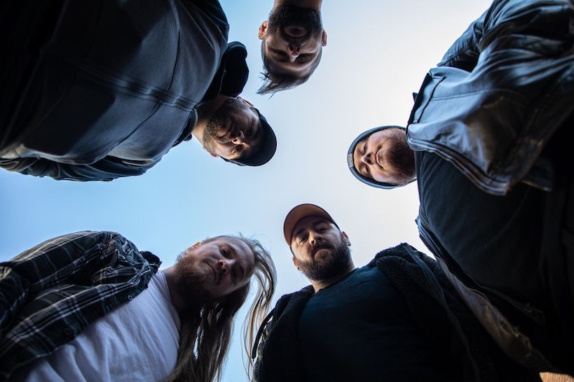 A group of five people looking down at the camera in a circle against a blue sky backdrop.
