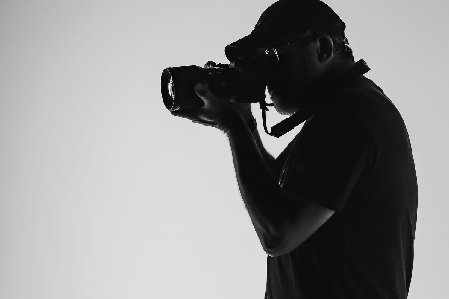 A silhouetted photographer takes a shot in profile view against a light background.