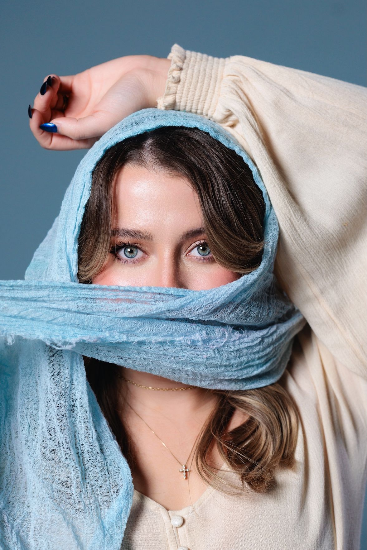 Creative portrait with light blue fabric draped around head against blue background.