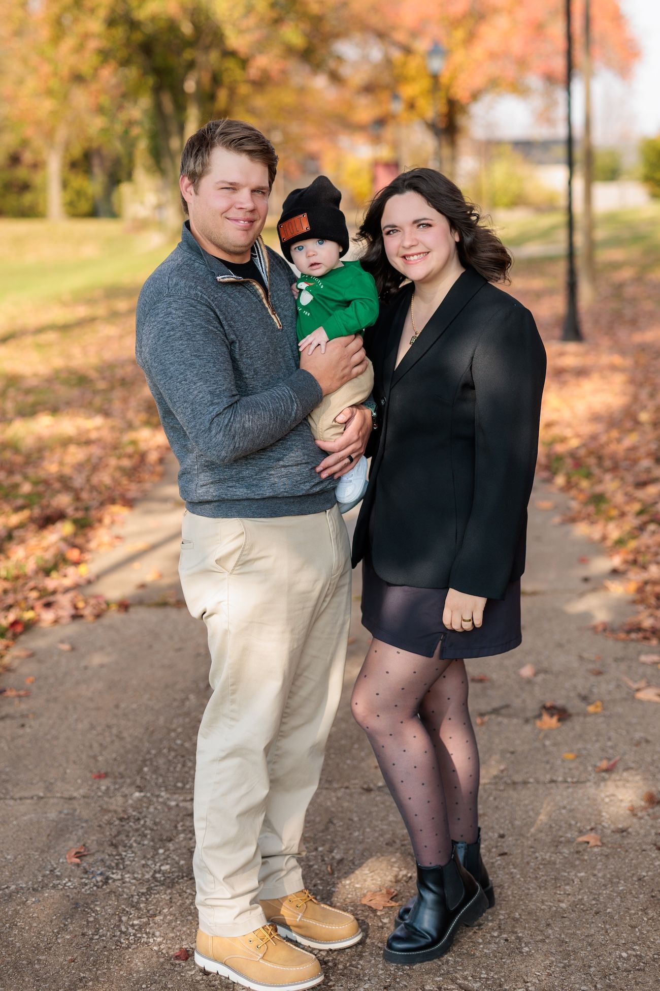 A family stands together on an autumn path lined with colorful fall foliage.