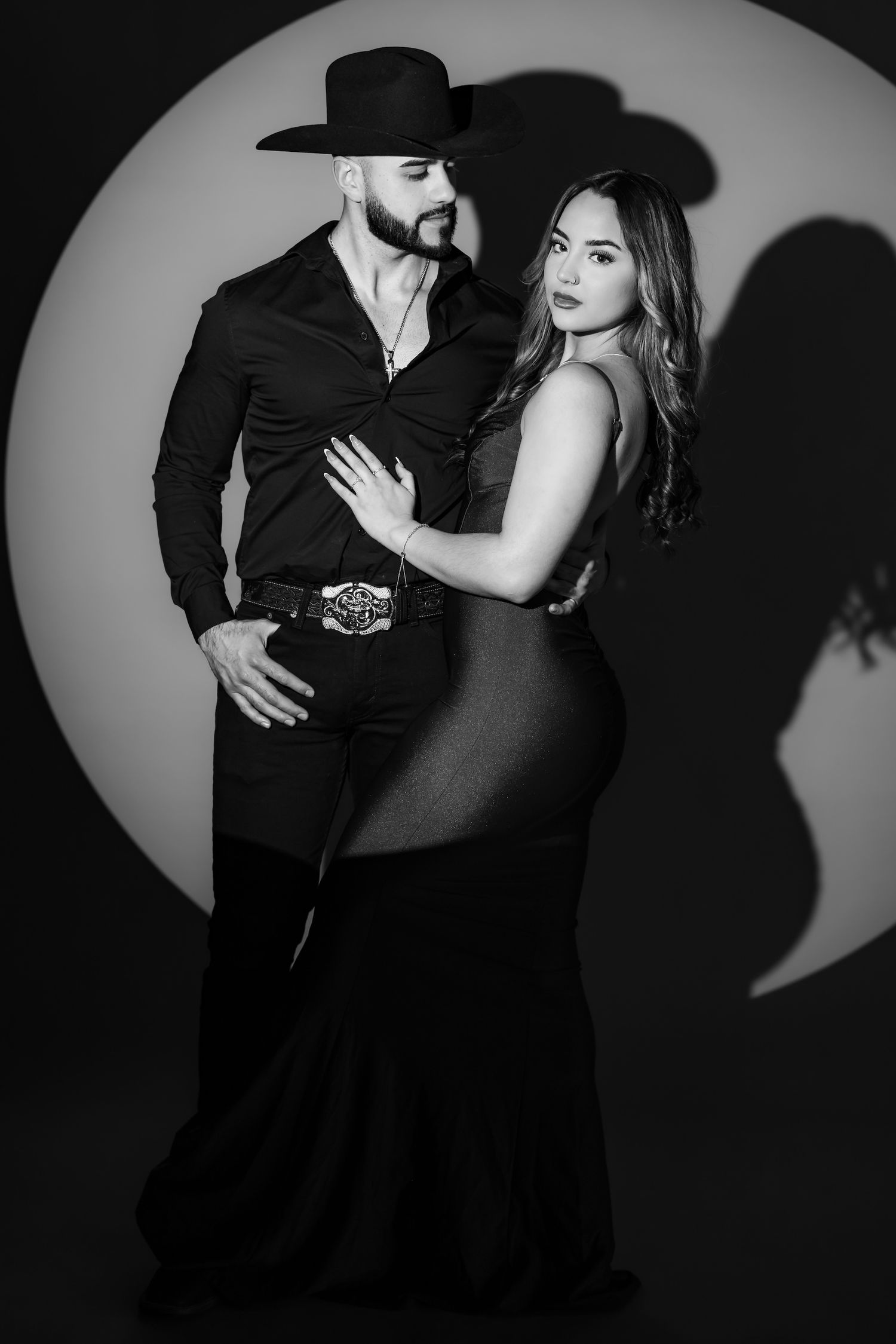 A romantic black and white portrait of a couple in formal western wear posing together against a circular backdrop.
