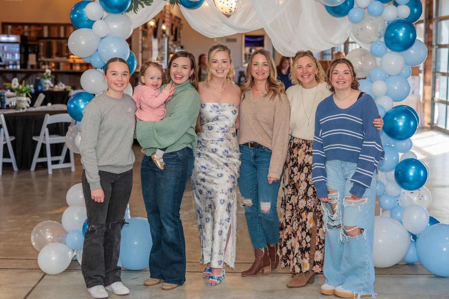 A group poses together under a decorative blue and white balloon arch at a festive celebration event.