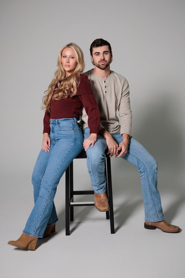 Two people in casual attire posing on a high stool against a grey studio backdrop.