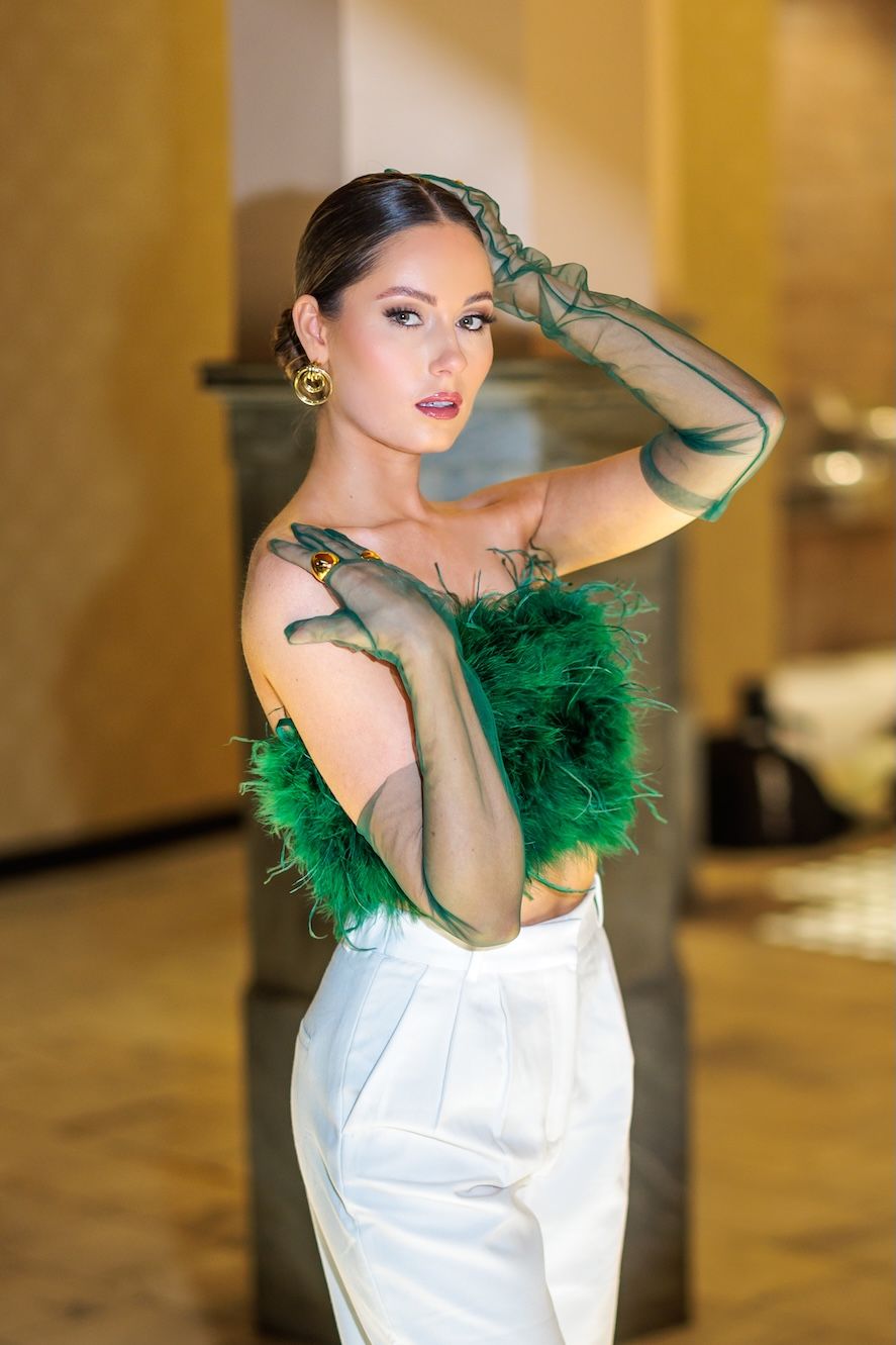 Elegant fashion photo featuring emerald green feathers and long gloves paired with a white formal dress in luxurious setting.
