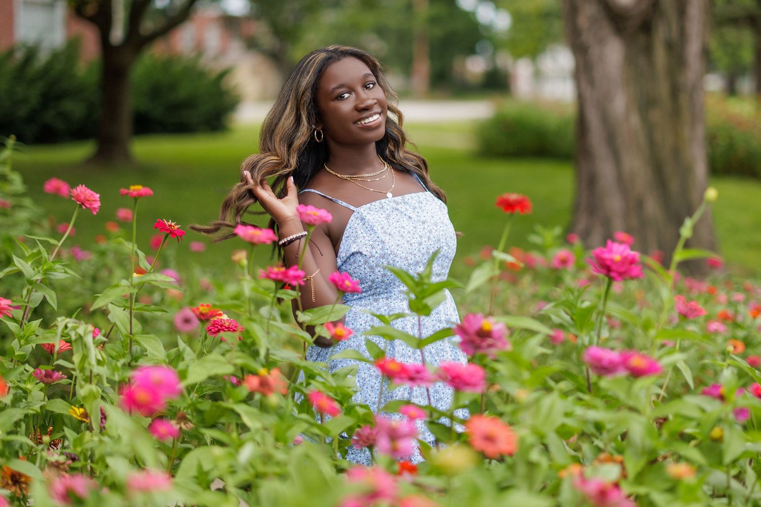 A woman in a white lace dress stands among vibrant pink flowers in a garden setting.