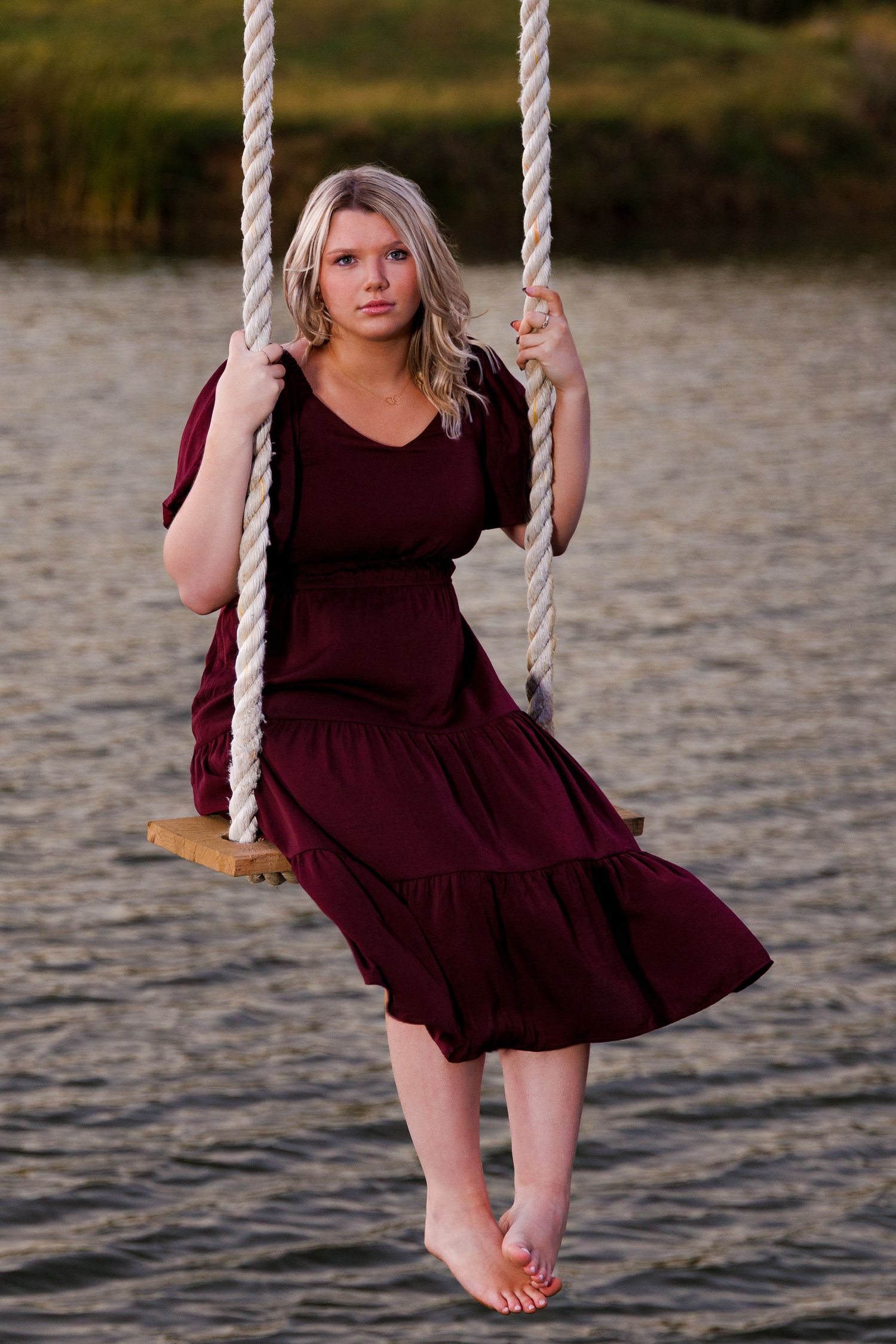 A person in a burgundy dress sits on a rope swing over water at sunset in a series of progressive motion shots.