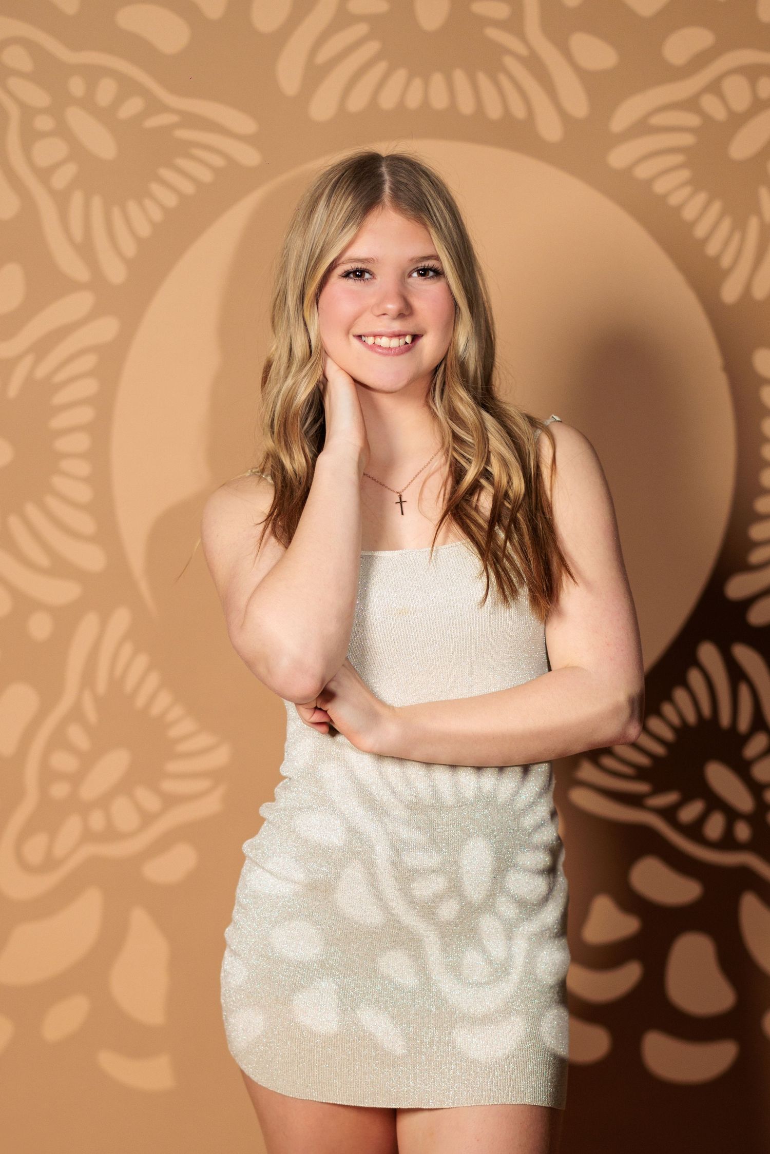 A person in a white sequined mini dress poses against a brown backdrop with decorative shadow patterns.