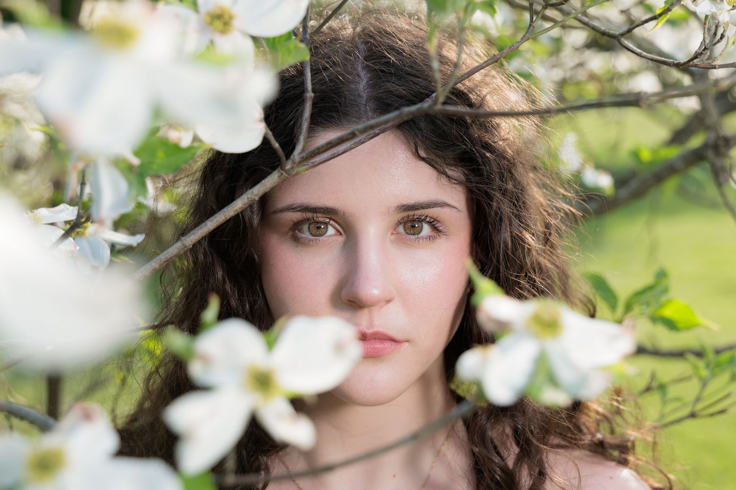 Dreamy springtime portrait surrounded by delicate white dogwood blossoms in a garden setting.