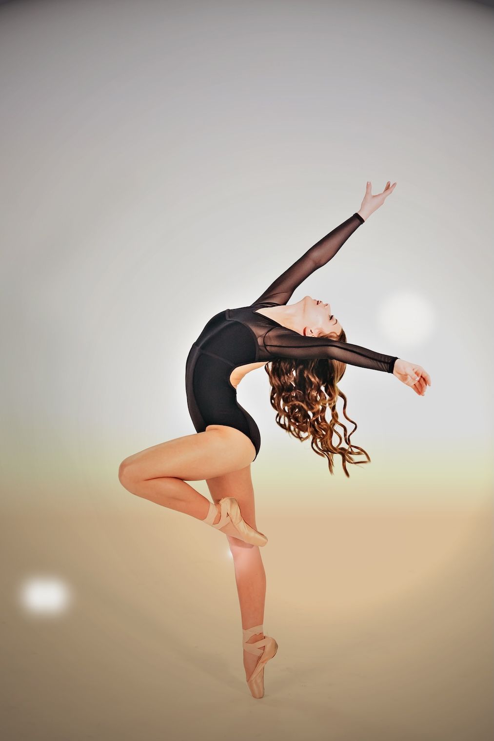 A graceful dancer in a black leotard performs an elegant backbend pose with flowing curly hair.