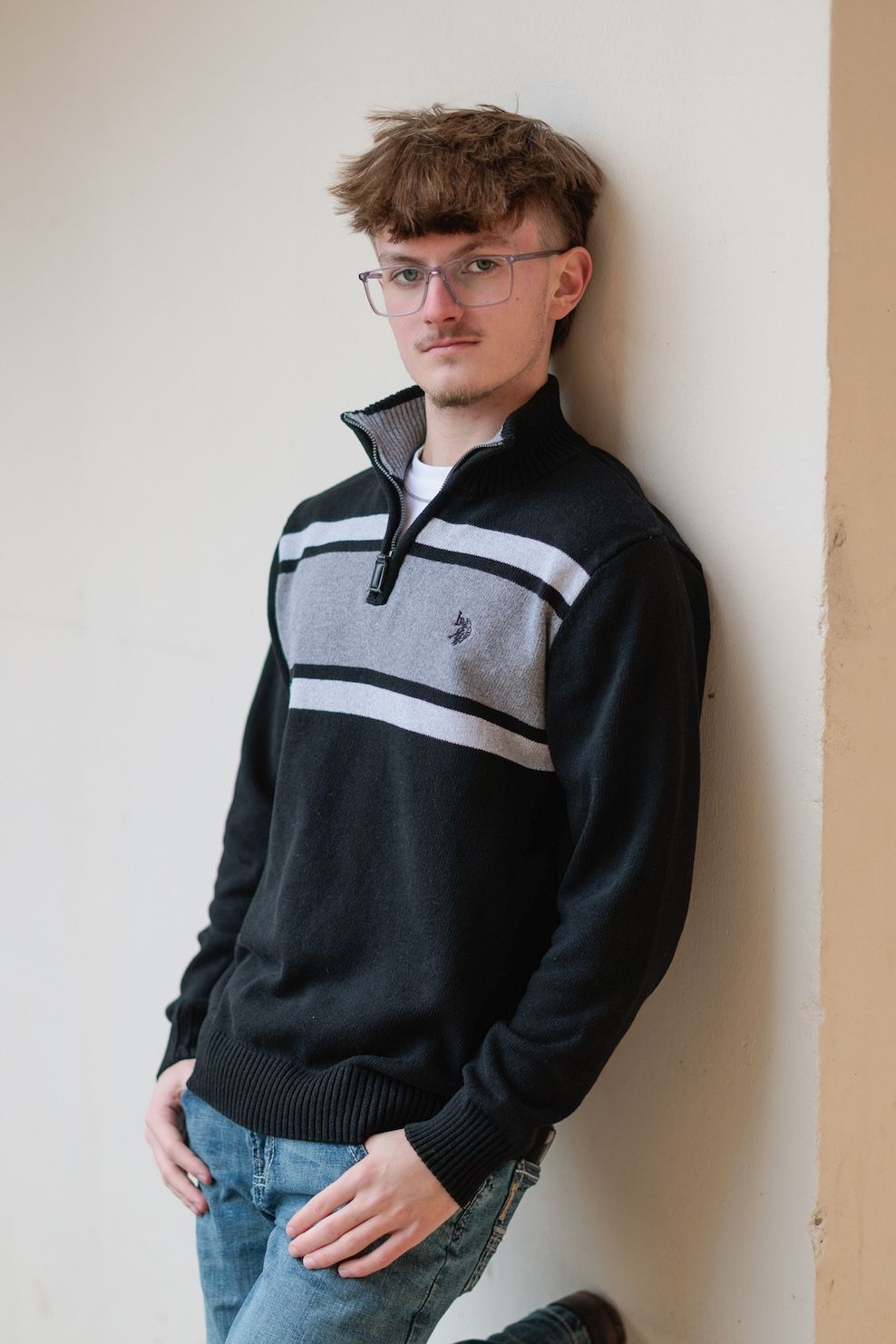 Portrait of person wearing black and gray quarter-zip pullover sweater with glasses against light colored wall.