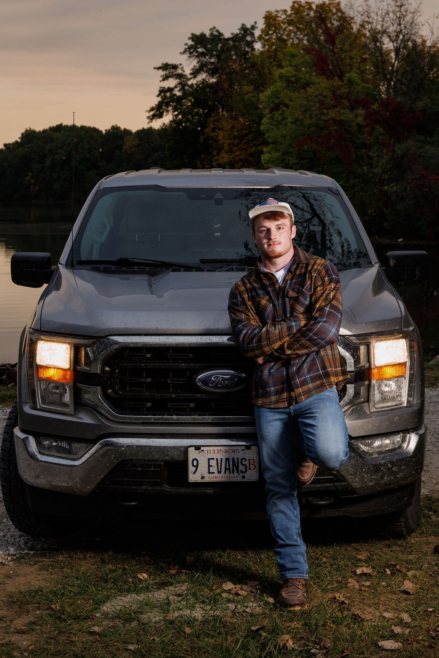 A black Ford pickup truck is parked at dusk with its headlights illuminated while someone leans against the front.