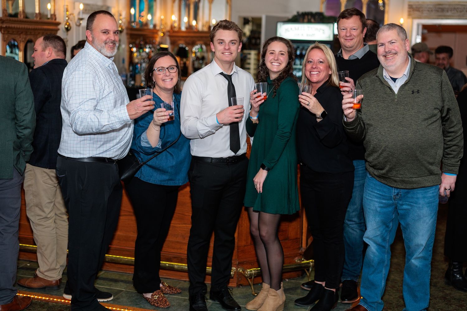 A group of people celebrating at an indoor party, raising drinks and smiling together in a festive atmosphere.