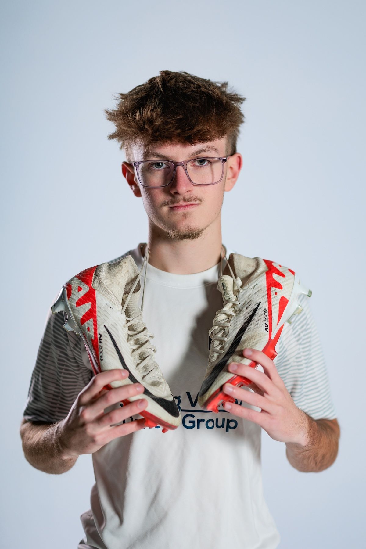 A person wearing glasses holds up a pair of athletic shoes against a light background.