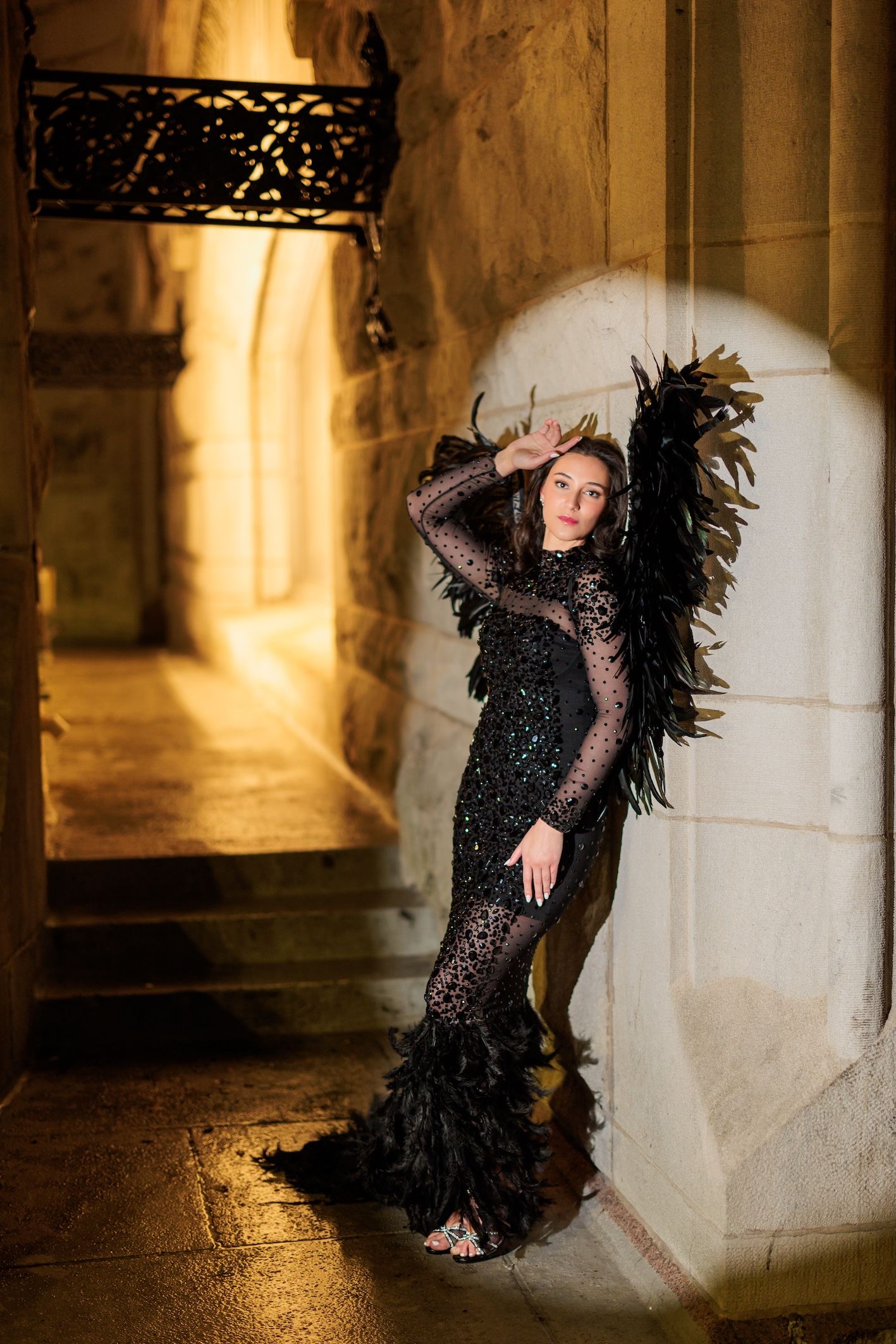 A dramatic fashion photo features a black sequined gown with feathers in a gothic archway setting.