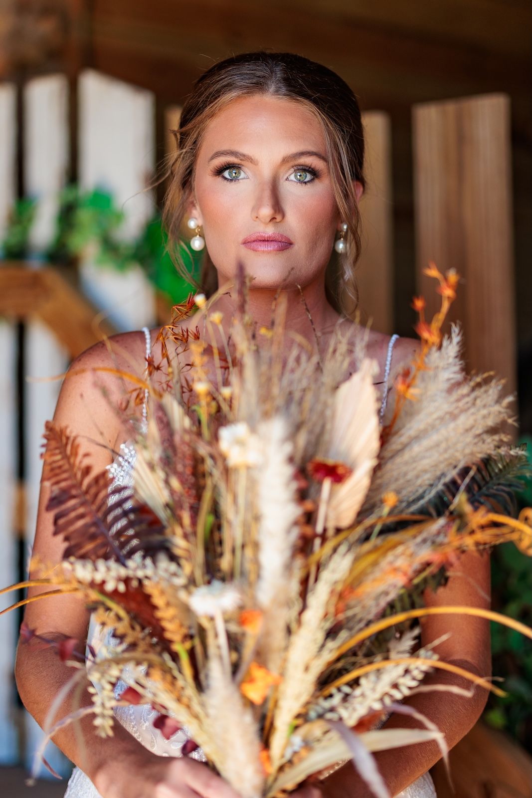 Elegant wedding photo featuring dried pampas grass and feather bouquet with dangling pearl earrings in warm indoor lighting.