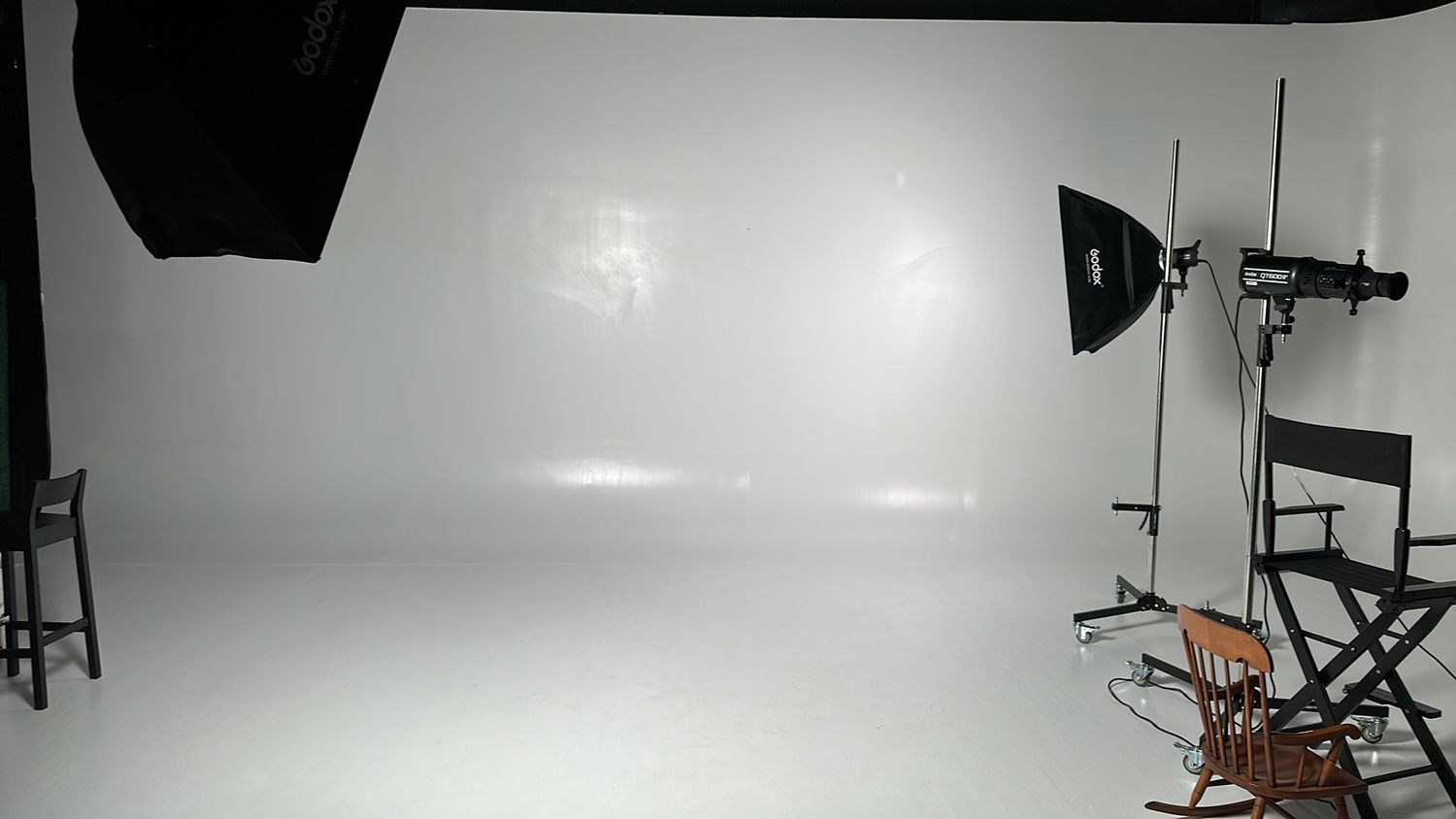 Professional photography studio setup with white backdrop, lighting equipment, and director's chair visible.