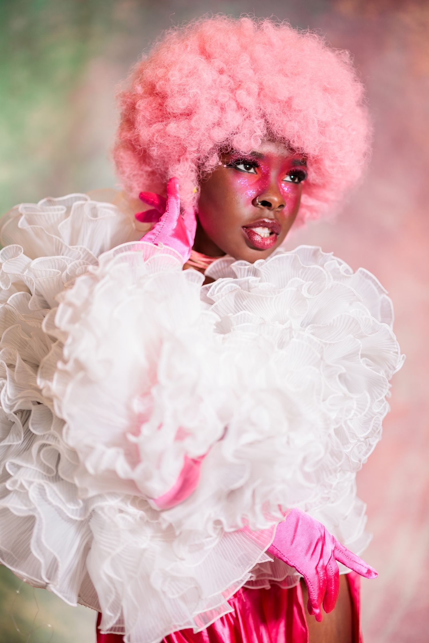 Fashion portrait featuring bright pink afro hairstyle and white ruffled dress with pink gloves in dreamy lighting.