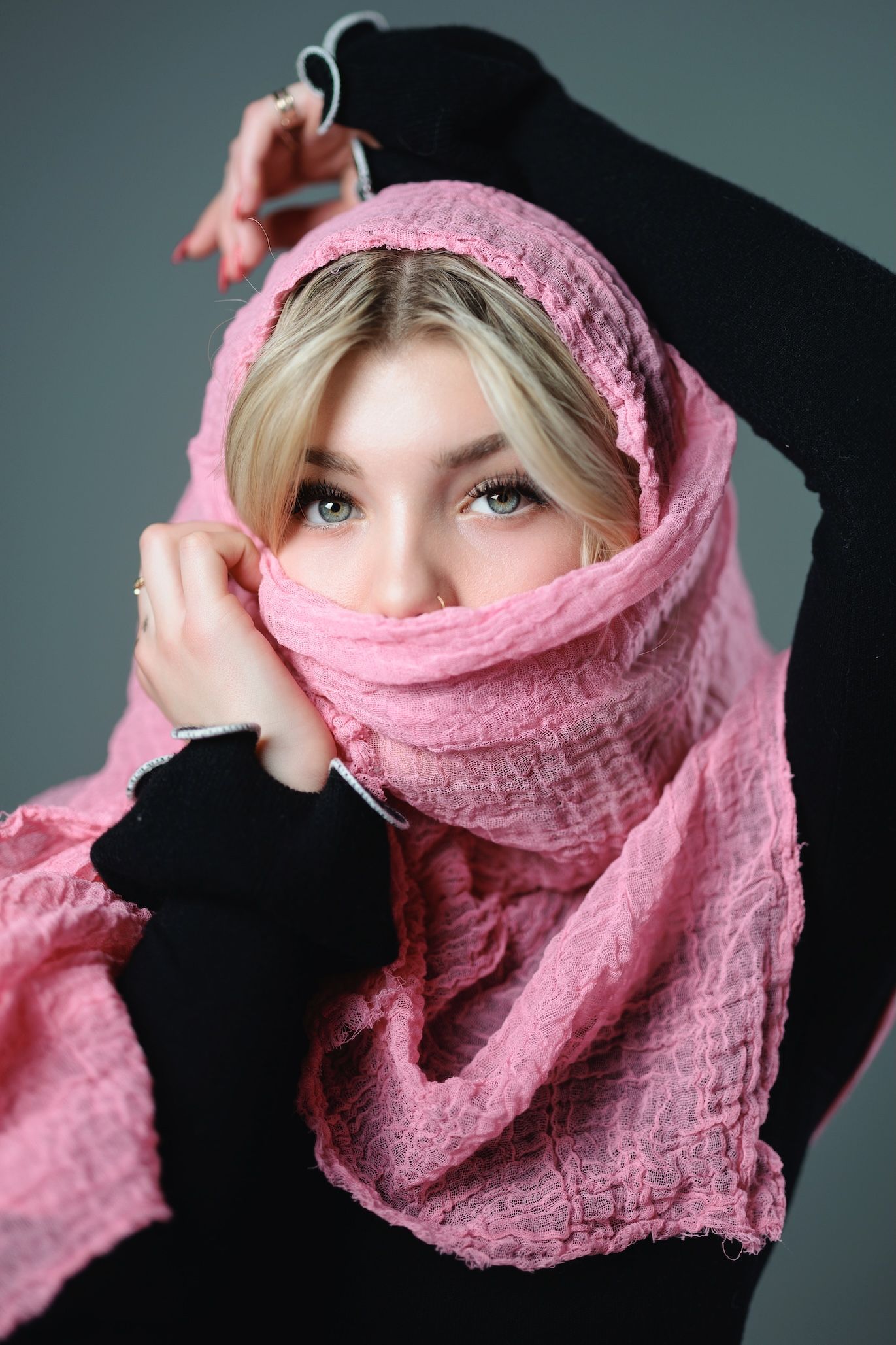 A portrait with pink fabric draped around the head against a studio backdrop with black sleeves visible.