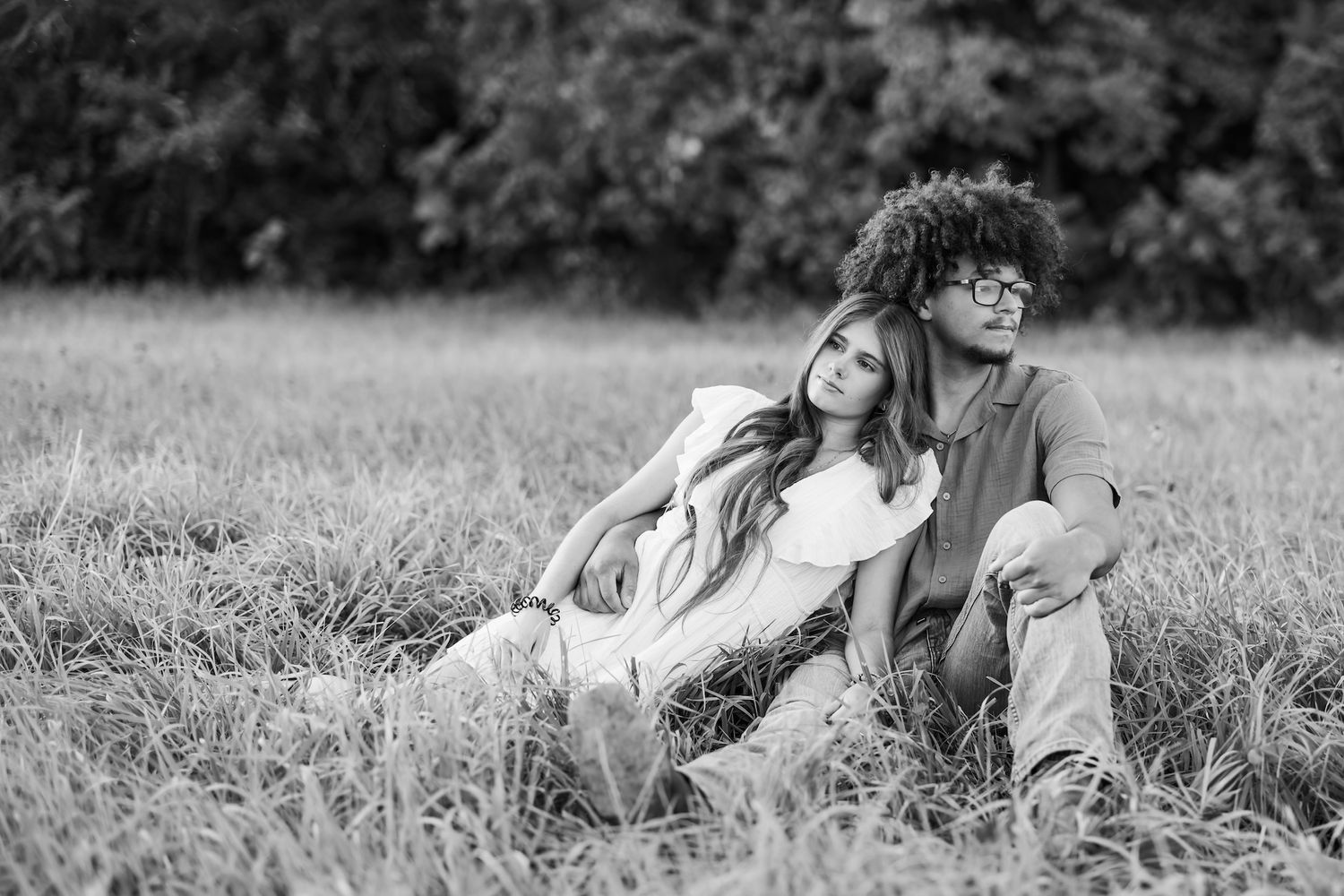 Black and white photo of a couple sitting together in a grassy field on a romantic afternoon.