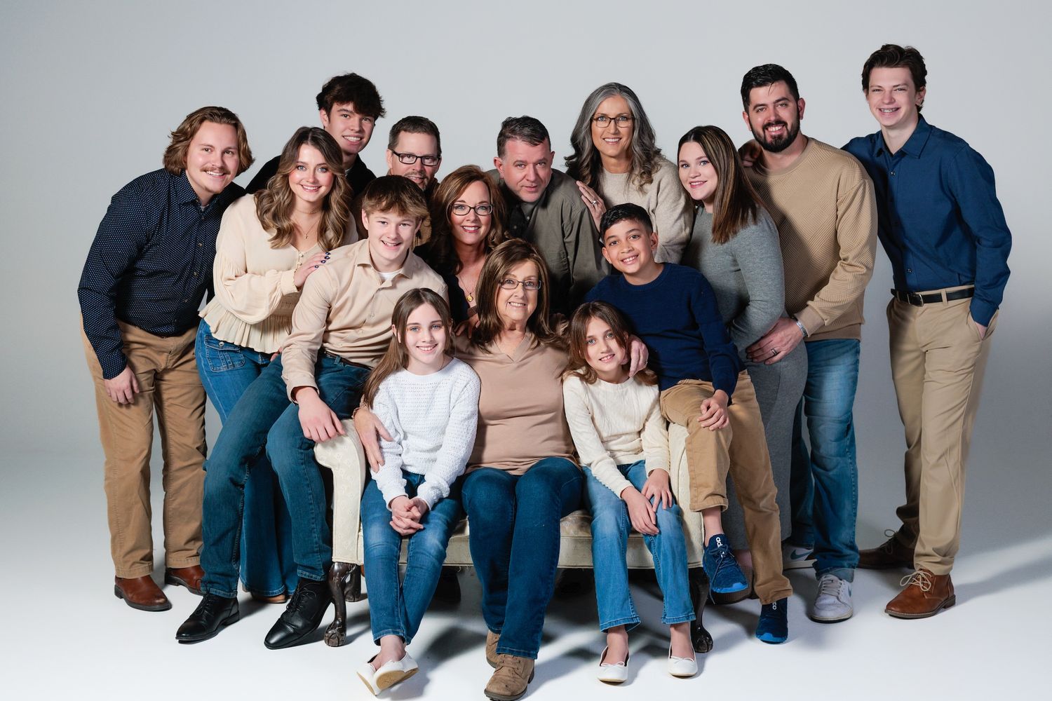 Studio portrait of a large family group wearing coordinated neutral tones against a white backdrop.