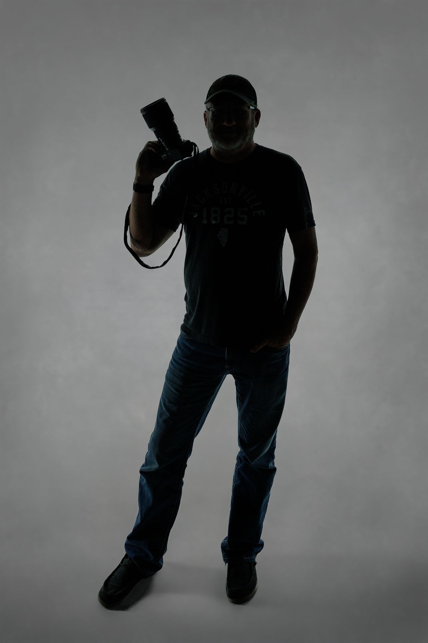 A silhouetted figure in jeans stands against a light background while holding a camera.