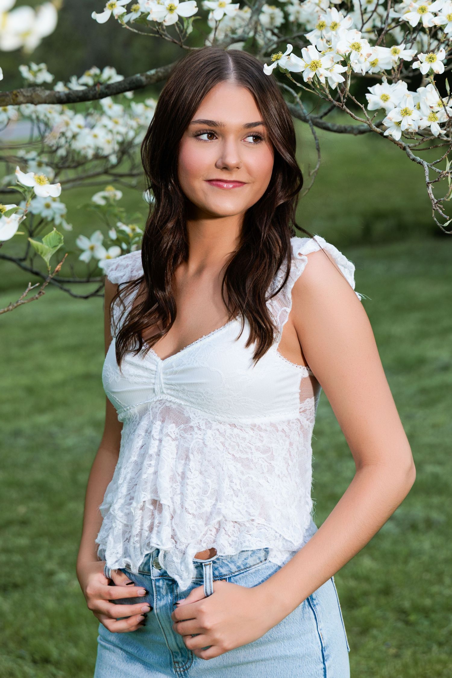 A springtime portrait under blooming white dogwood blossoms, wearing a white lace top and denim jeans.