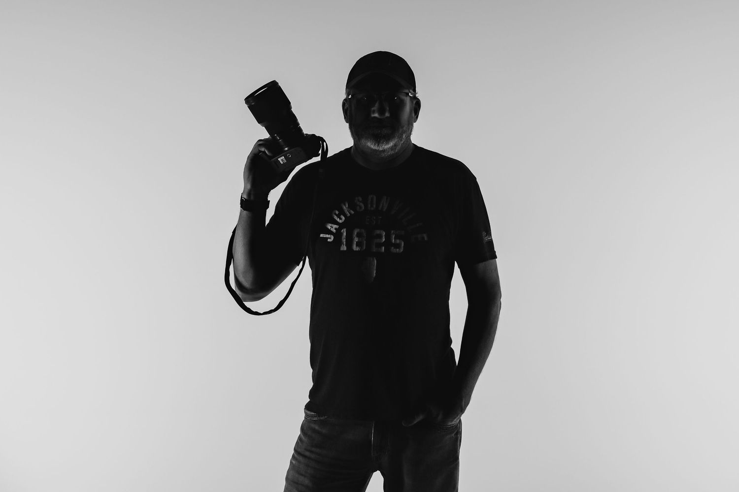 Silhouetted figure in dark clothing holds up a camera against a light background in high contrast black and white.