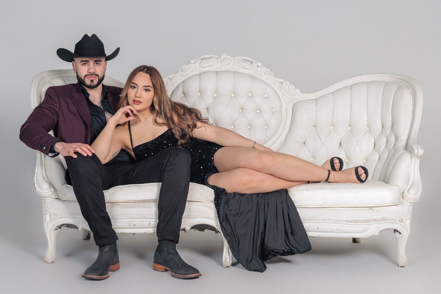 A couple poses together on an ornate white vintage sofa in a studio setting.