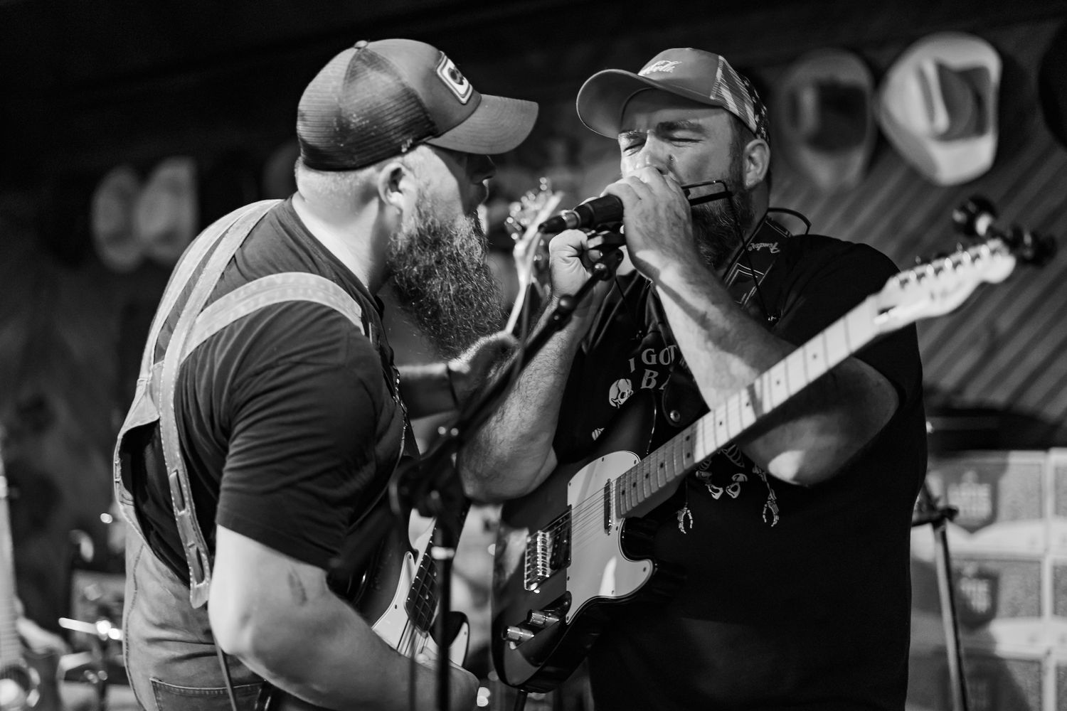 Black and white photo of two bearded performers on stage, one singing into microphone while other plays guitar.