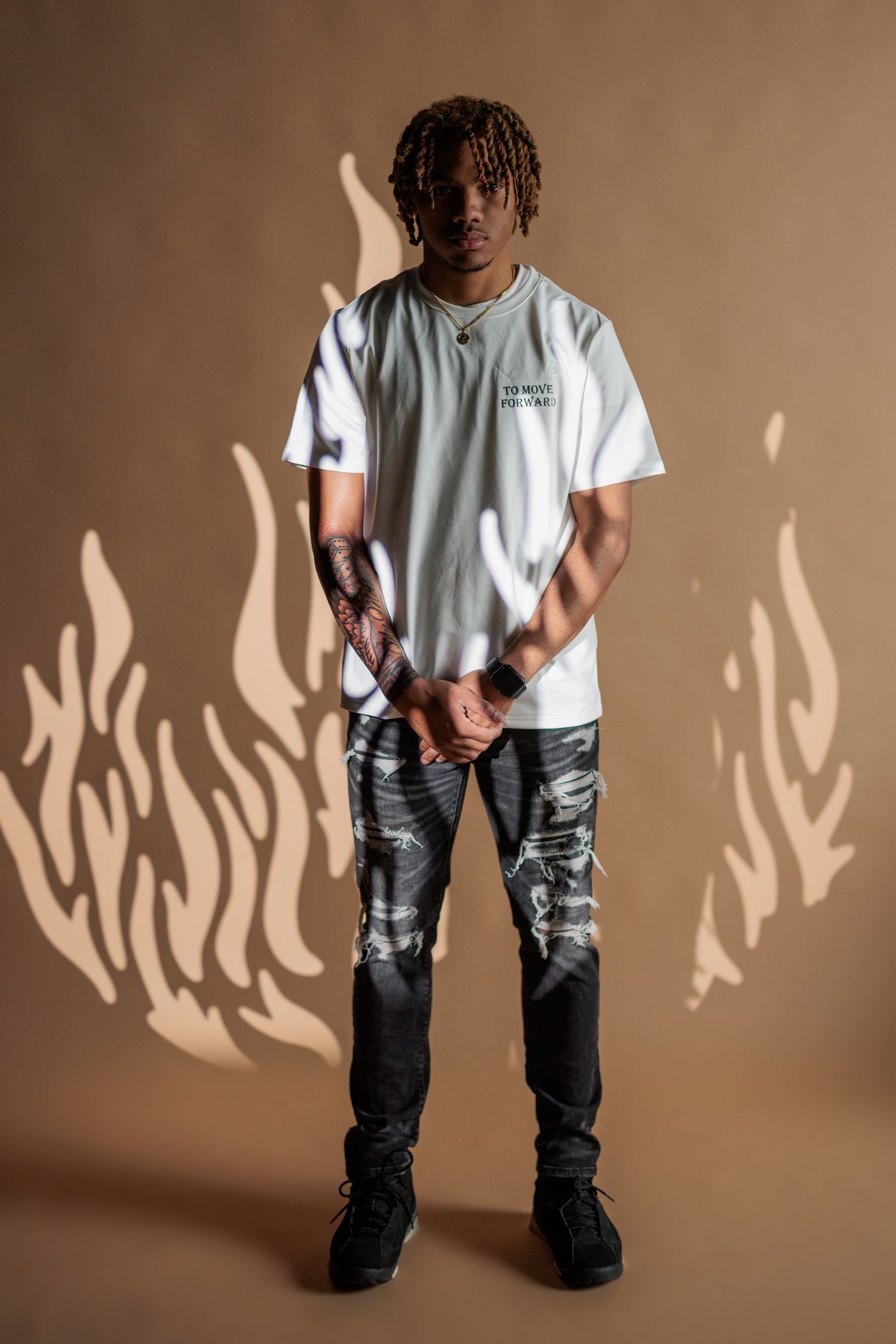 Street fashion portrait of someone in a white t-shirt and distressed camo cargo pants against a beige background.