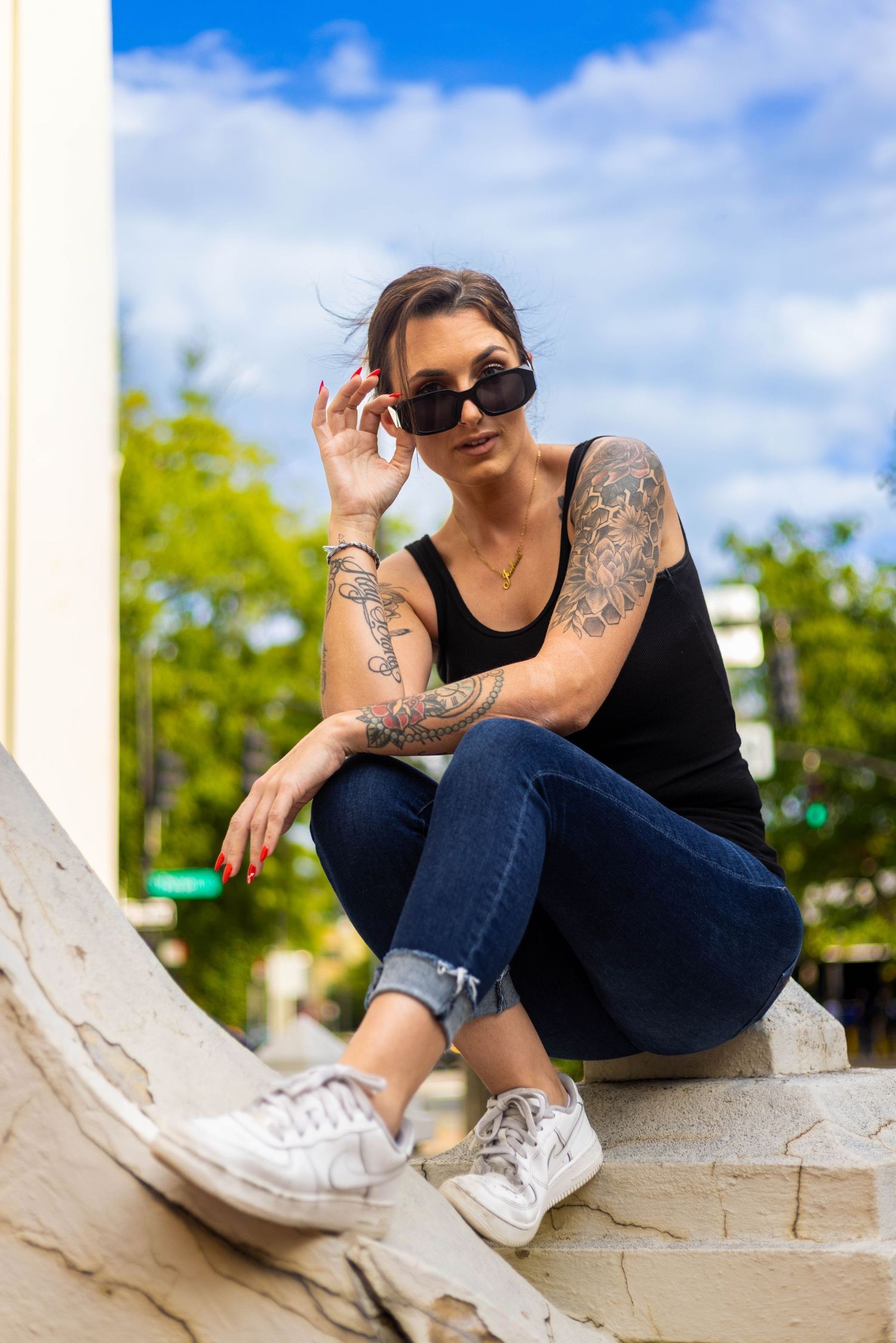Casual portrait of someone in sunglasses and jeans sitting on a white ledge outdoors. Portrava Creative Studios