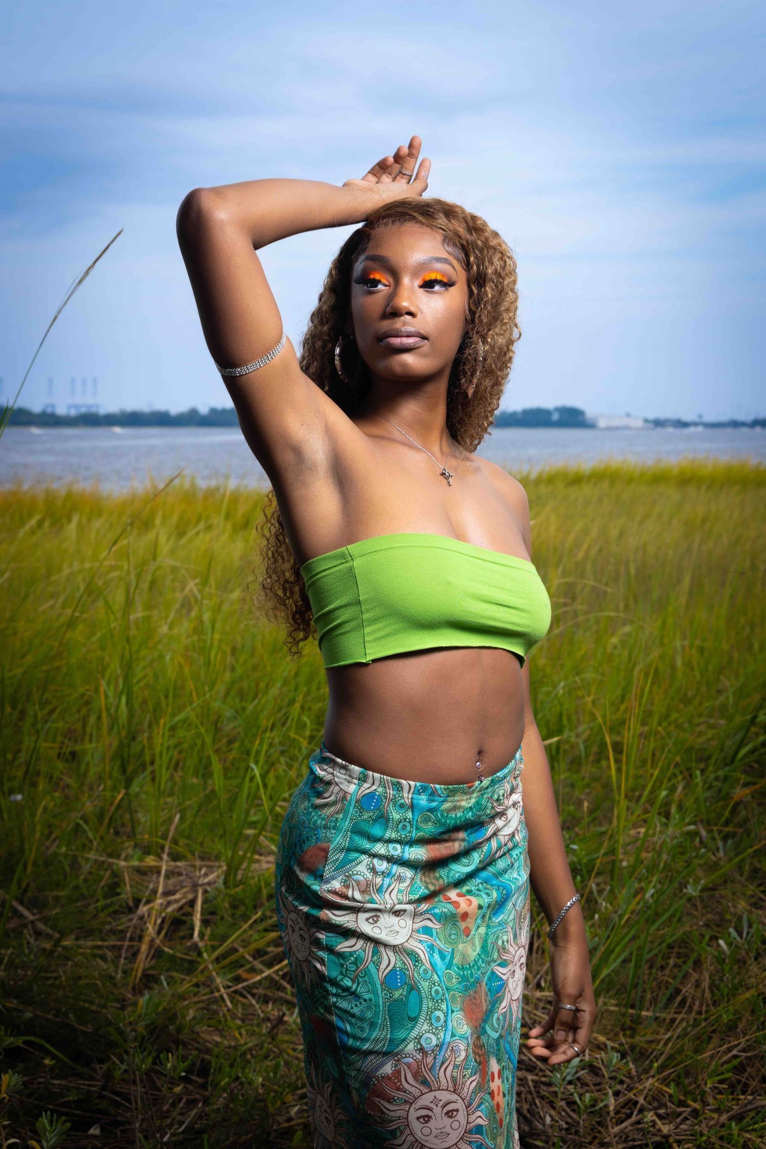 Model in lime green crop top and floral sarong poses elegantly against marsh background at sunset. Portrava Creative Studios