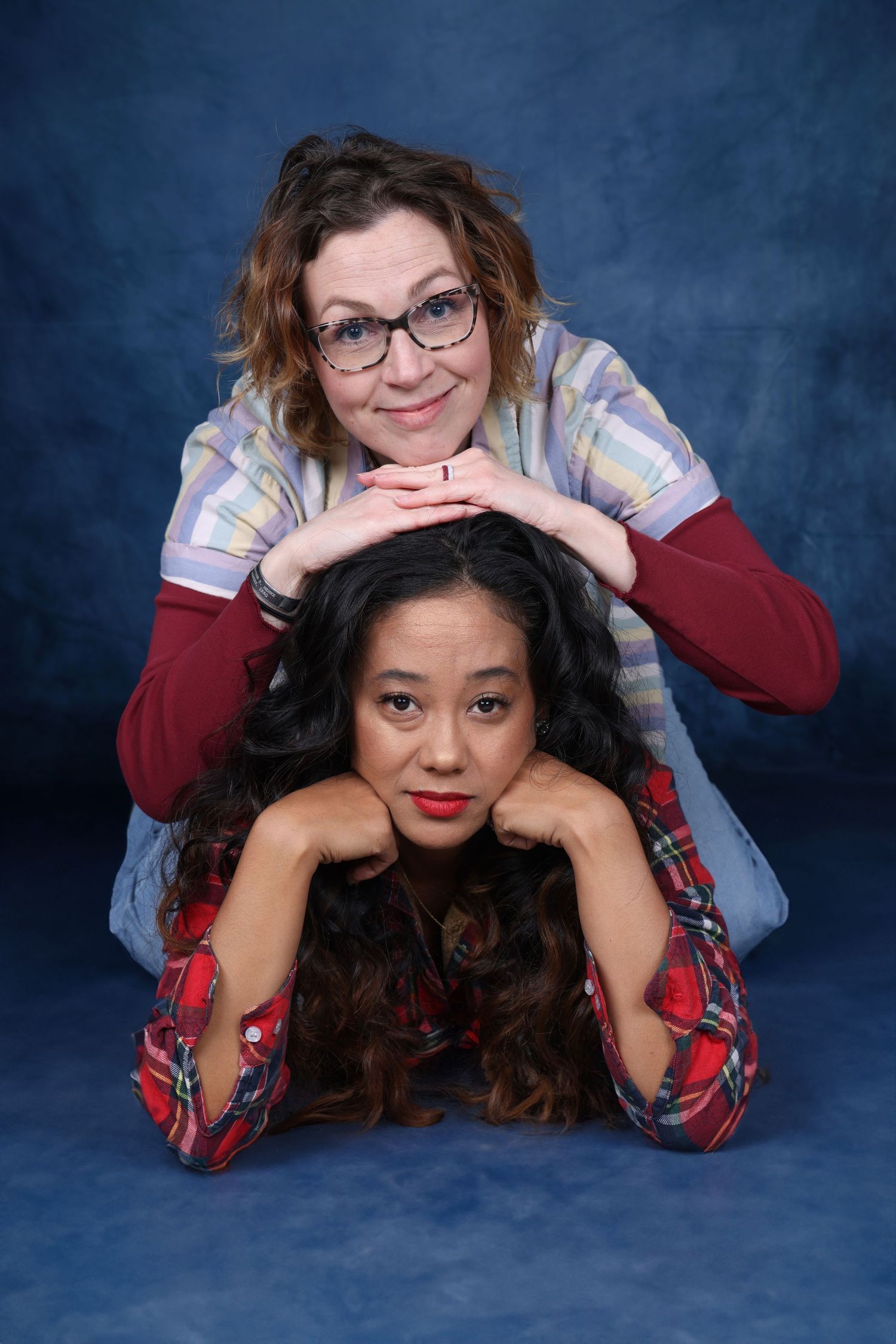 Two performers strike playful pose for studio portrait against blue backdrop. Portrava Creative Studios