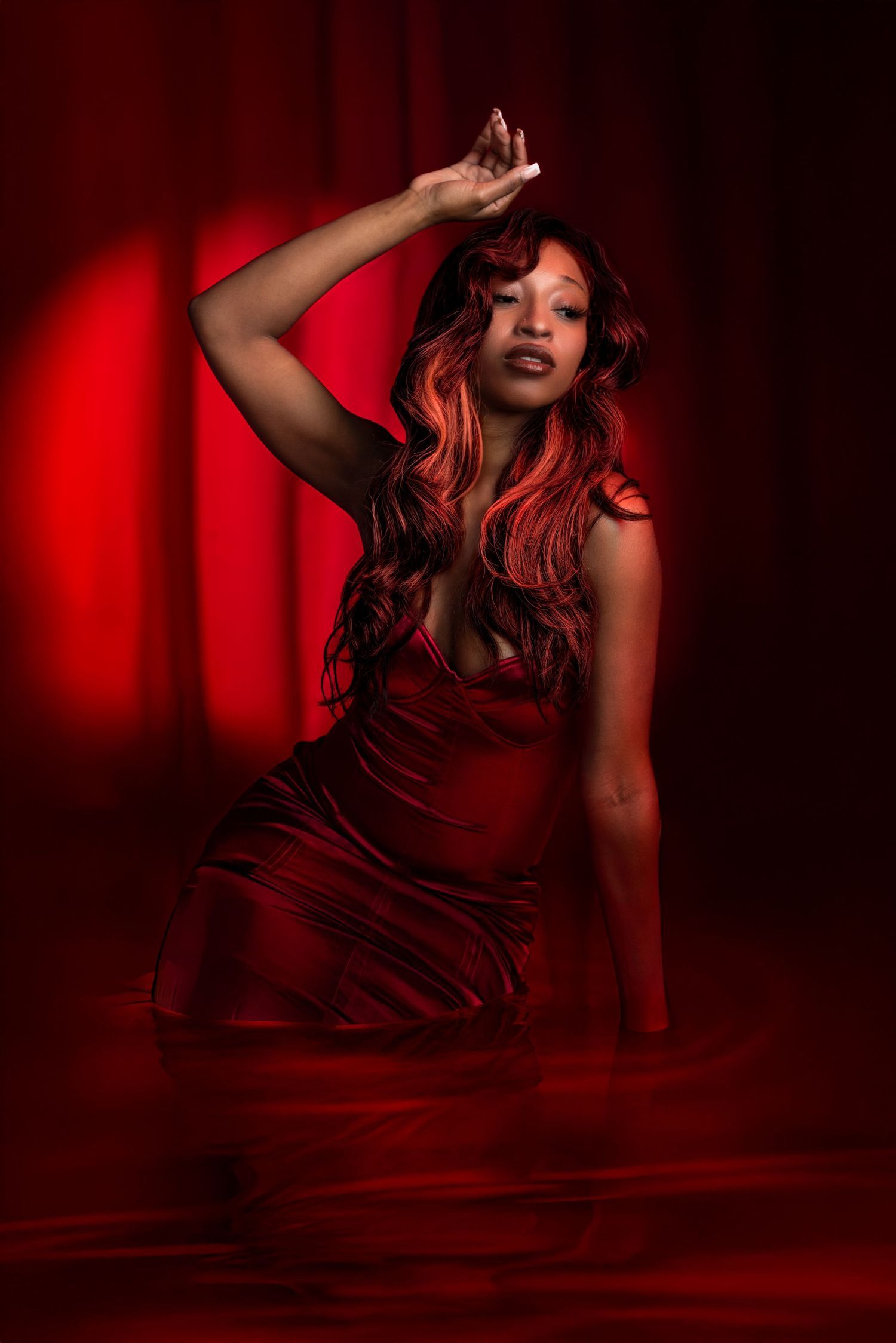Dramatic pose in red dress against deep crimson backdrop with theatrical lighting. Portrava Creative Studios