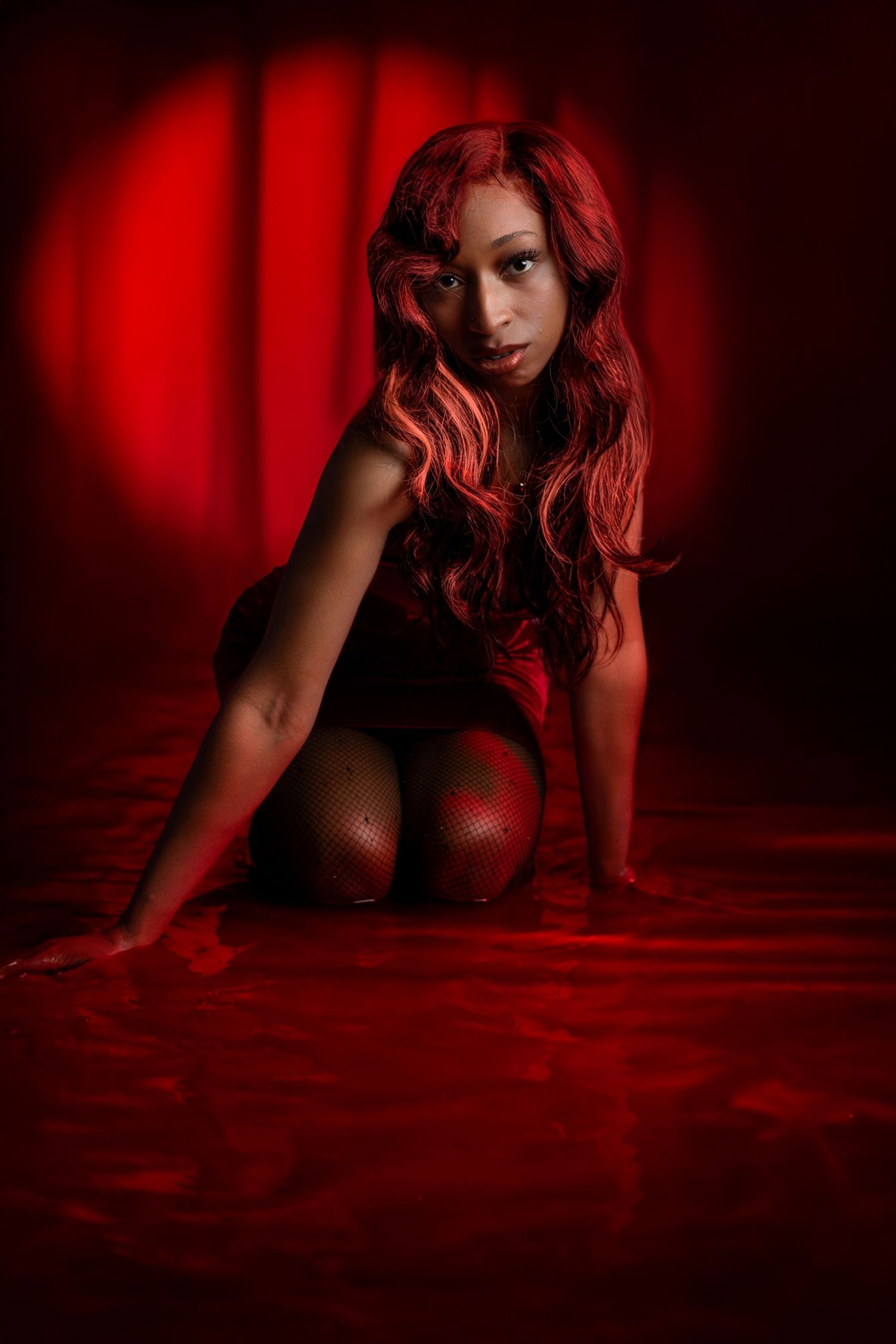 Artistic portrait with red hair in dramatic red lighting and dark setting.Portrava Creative Studios
