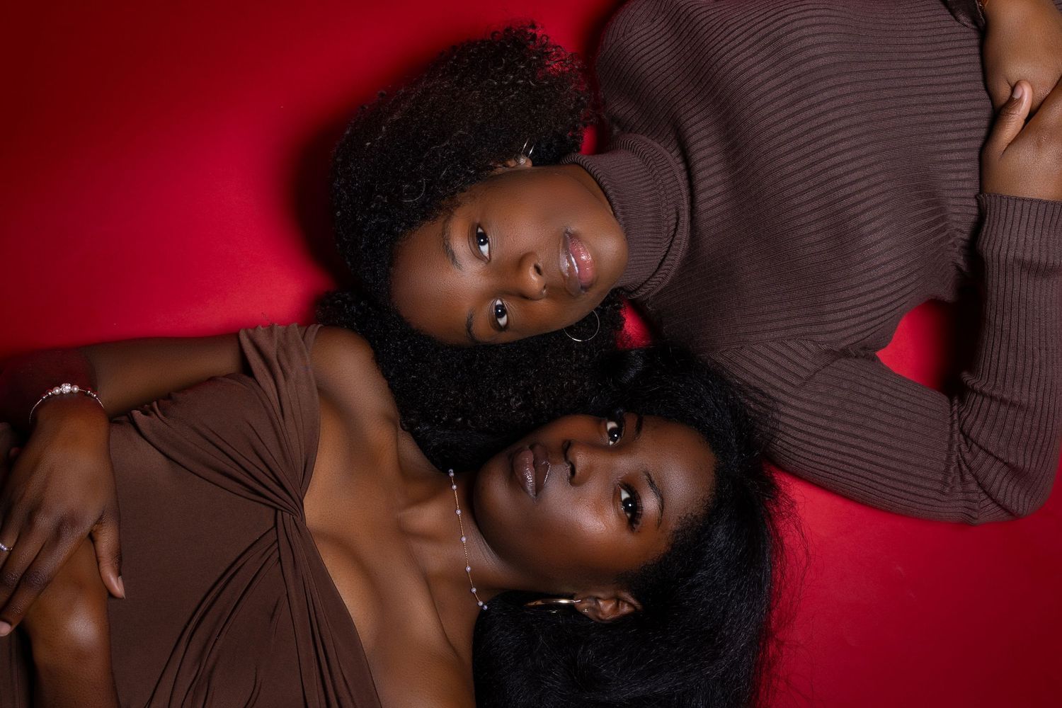Artistic portrait of two models in brown tops against red backdrop. Portrava Creative Studios