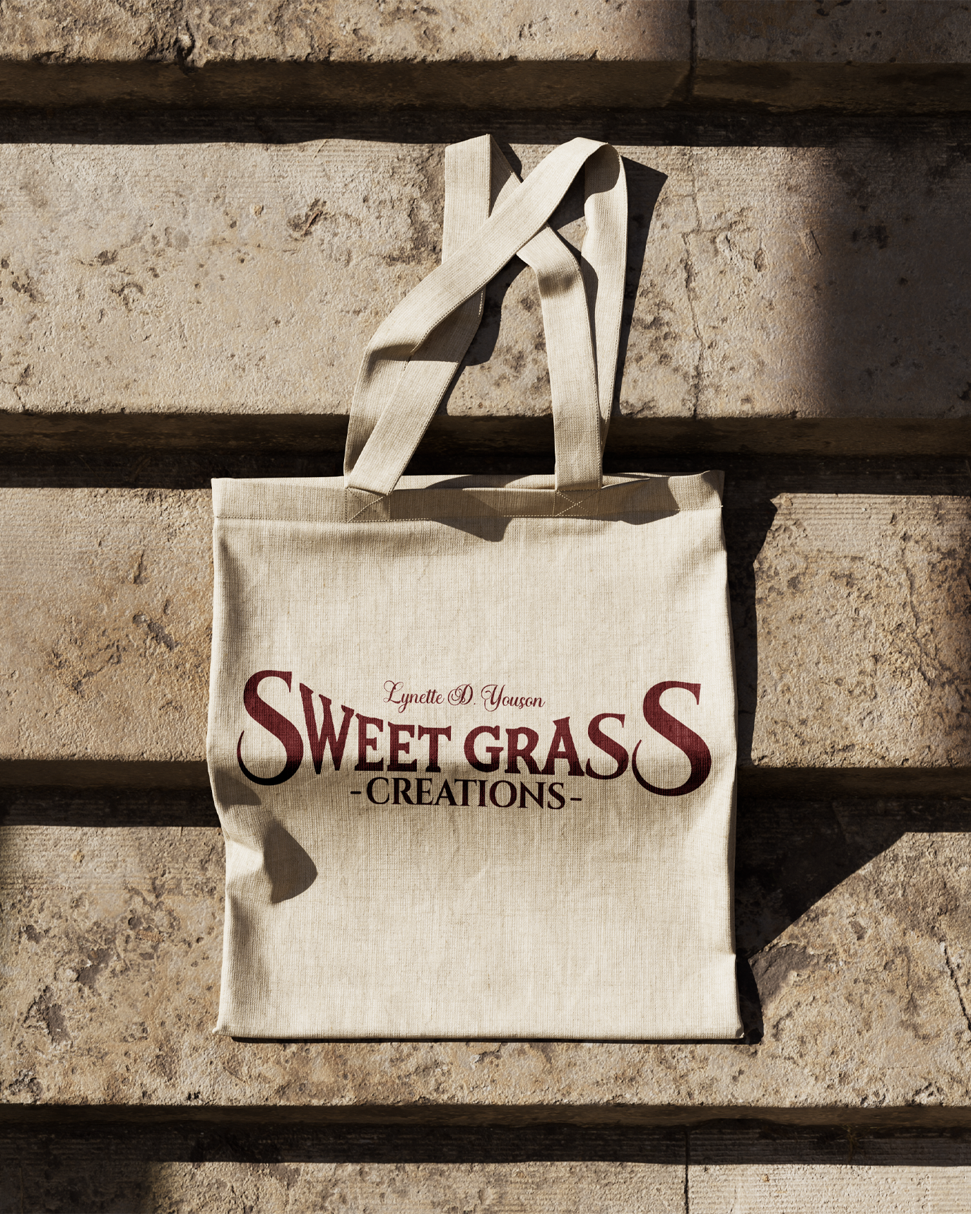 Canvas tote bag with Sweet Grass Creations logo hanging against textured wall. Portrava Creative Studios