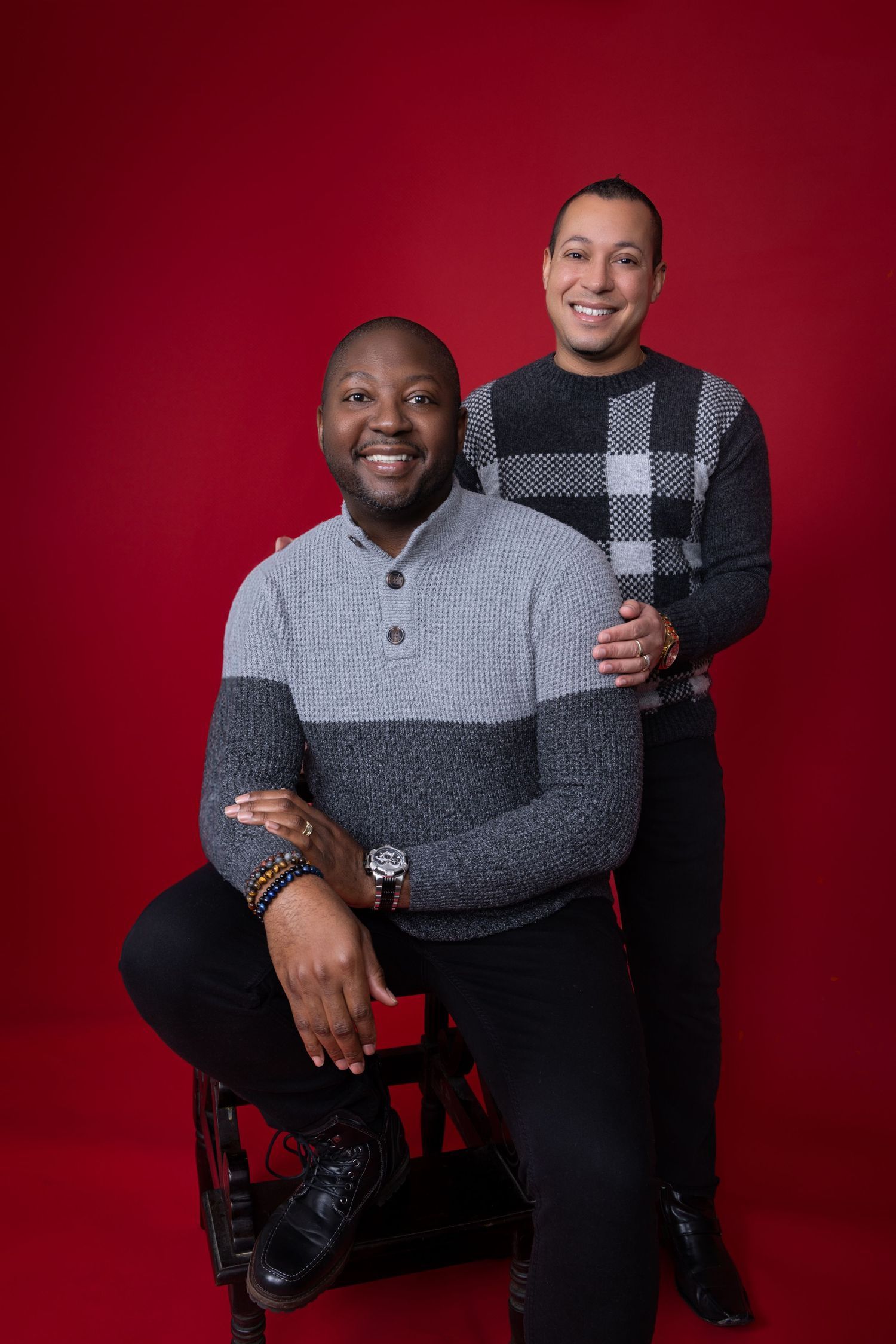 Studio portrait of two people in winter sweaters against red background. Portrava Creative Studios
