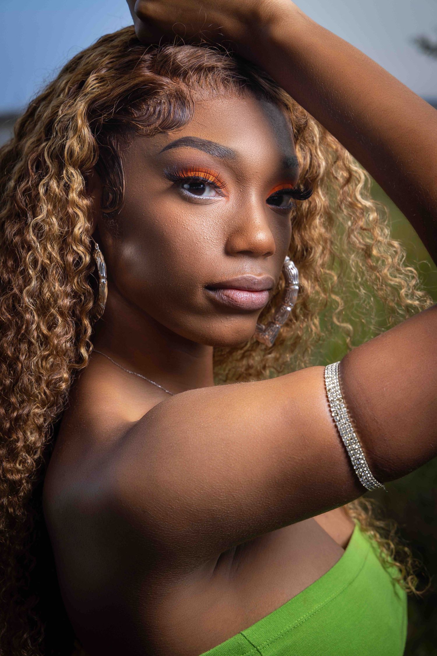 Portrait of person with honey-blonde curls wearing green top in outdoor setting. Portrava Creative Studios
