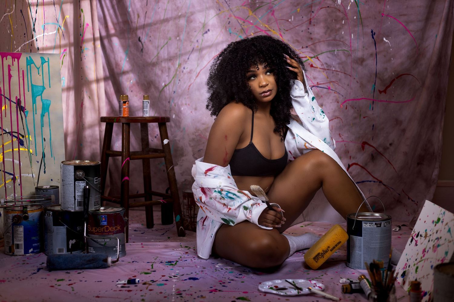 Creative portrait of a model in black lingerie against a paint splattered backdrop. Portrava Creative Studios