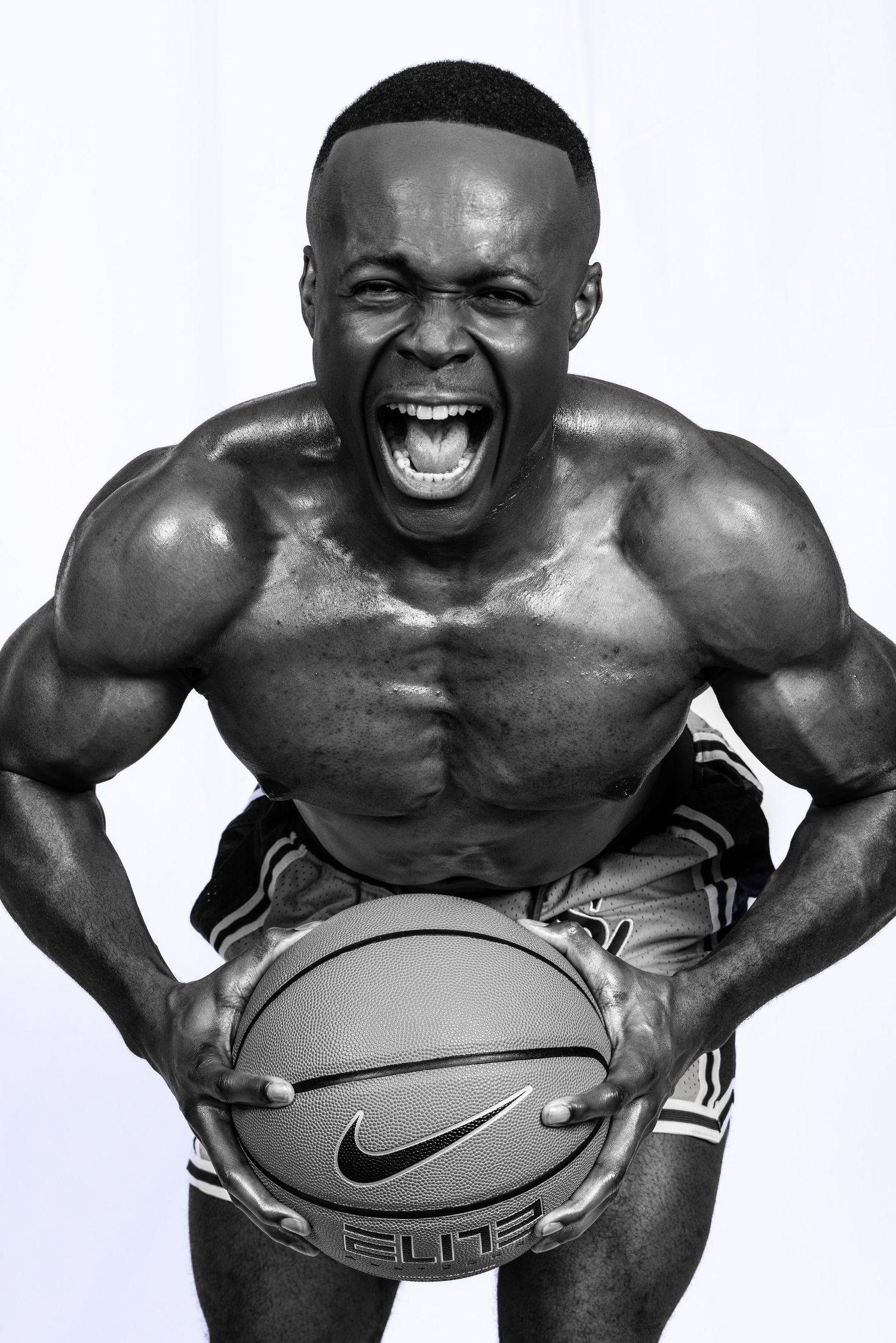 Athletic figure showing intense expression while holding basketball in dramatic black and white portrait. Portrava Creative Studios