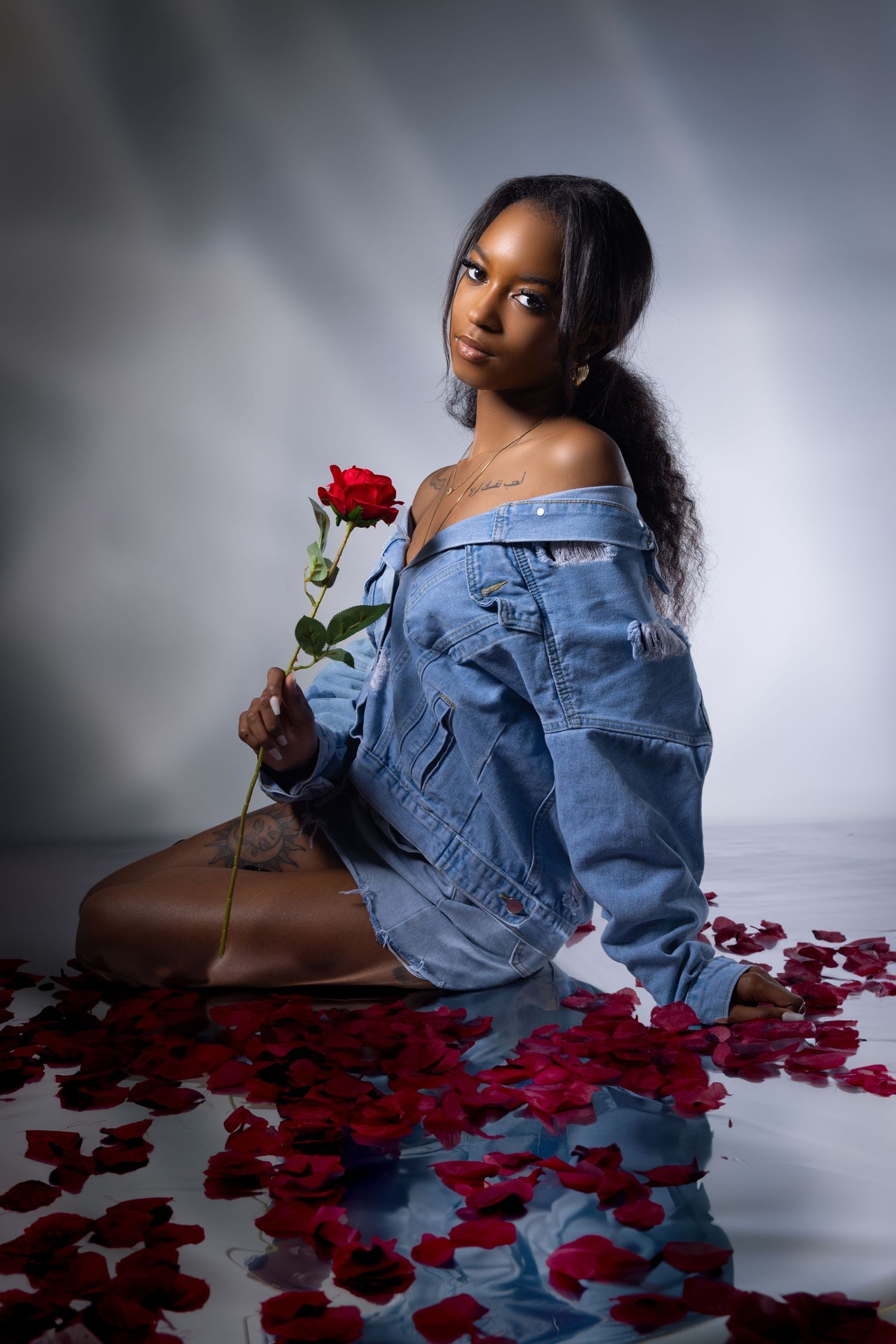 Dramatic portrait with red rose petals and denim jacket in studio lighting. Portrava Creative Studios