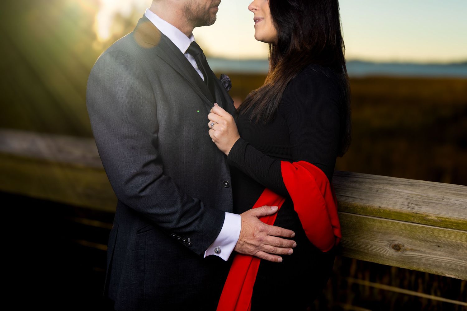 A romantic couple in formal attire shares an intimate moment during a sunset photoshoot by wooden railings.