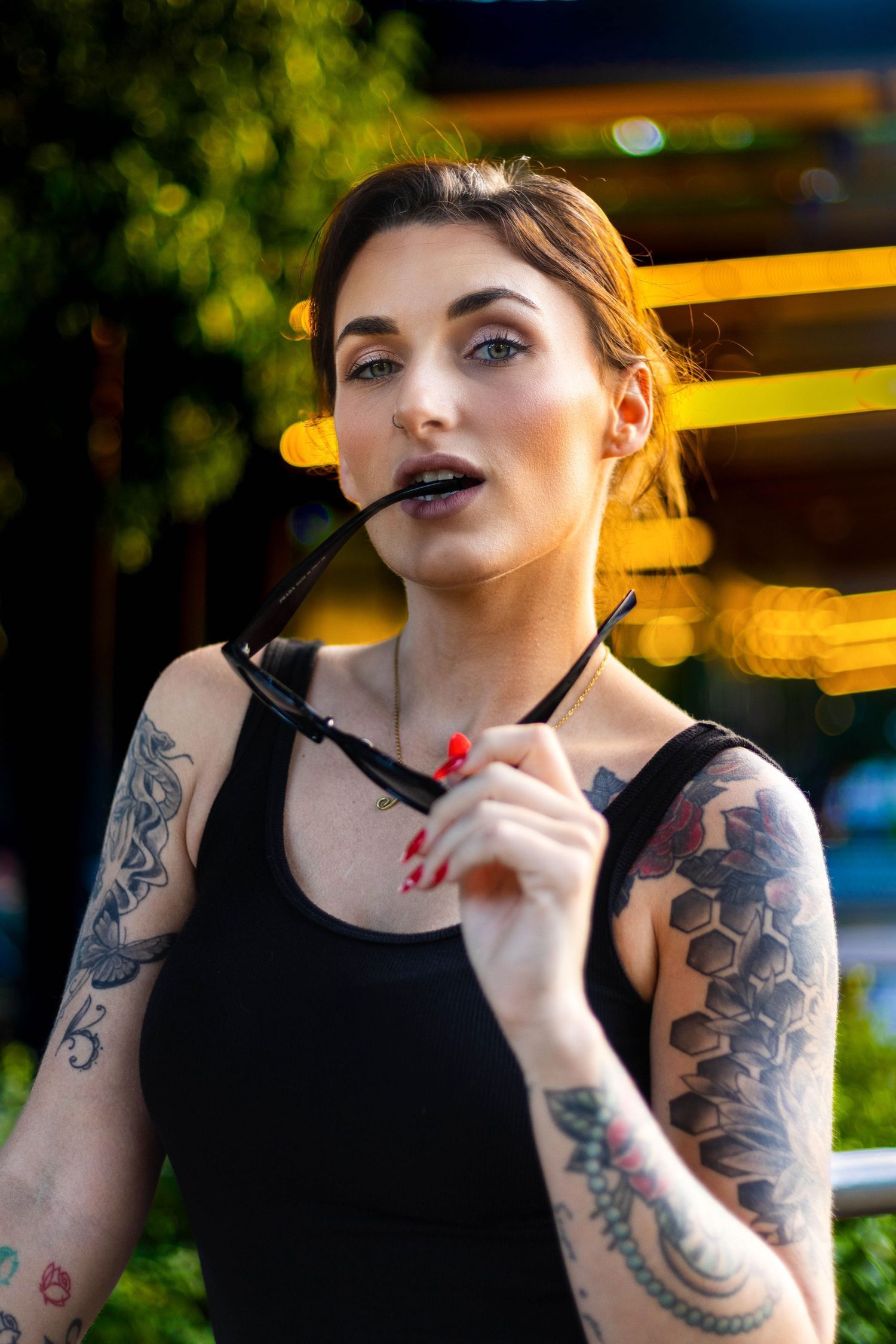 Close-up portrait with visible tattoos and dark lipstick against evening outdoor lighting. Portrava Creative Studios