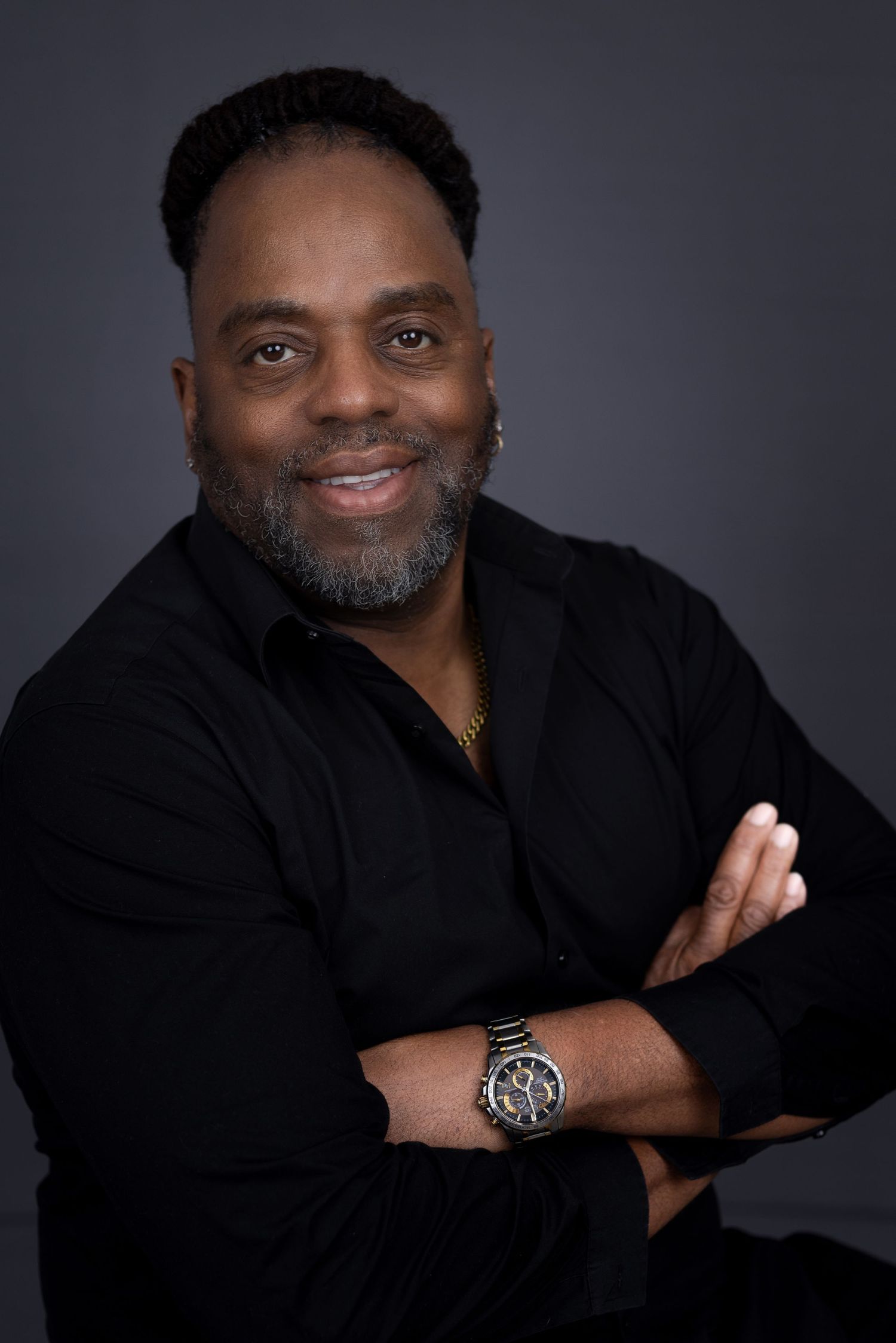 Professional headshot of man in black shirt with salt-and-pepper beard against dark background. Portrava Creative Studios