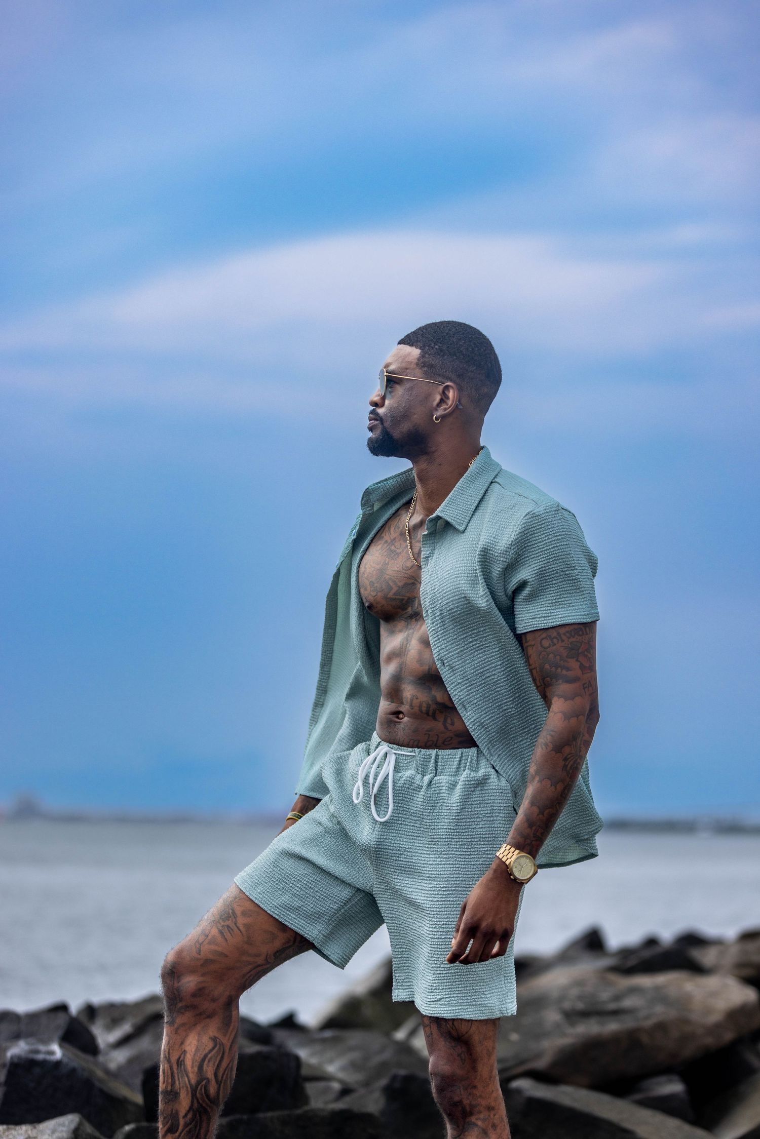 Athletic figure in sage green outfit posing on rocky beach. Portrava Creative Studios