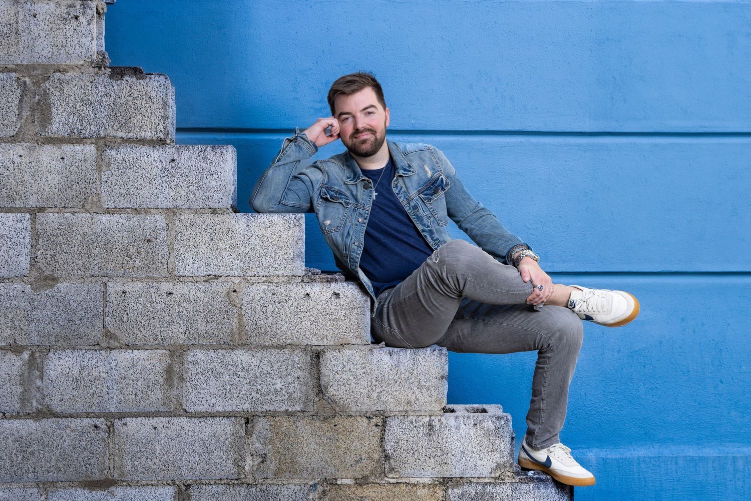 Casual portrait of person sitting on concrete steps against bright blue wall. Portrava Creative Studios